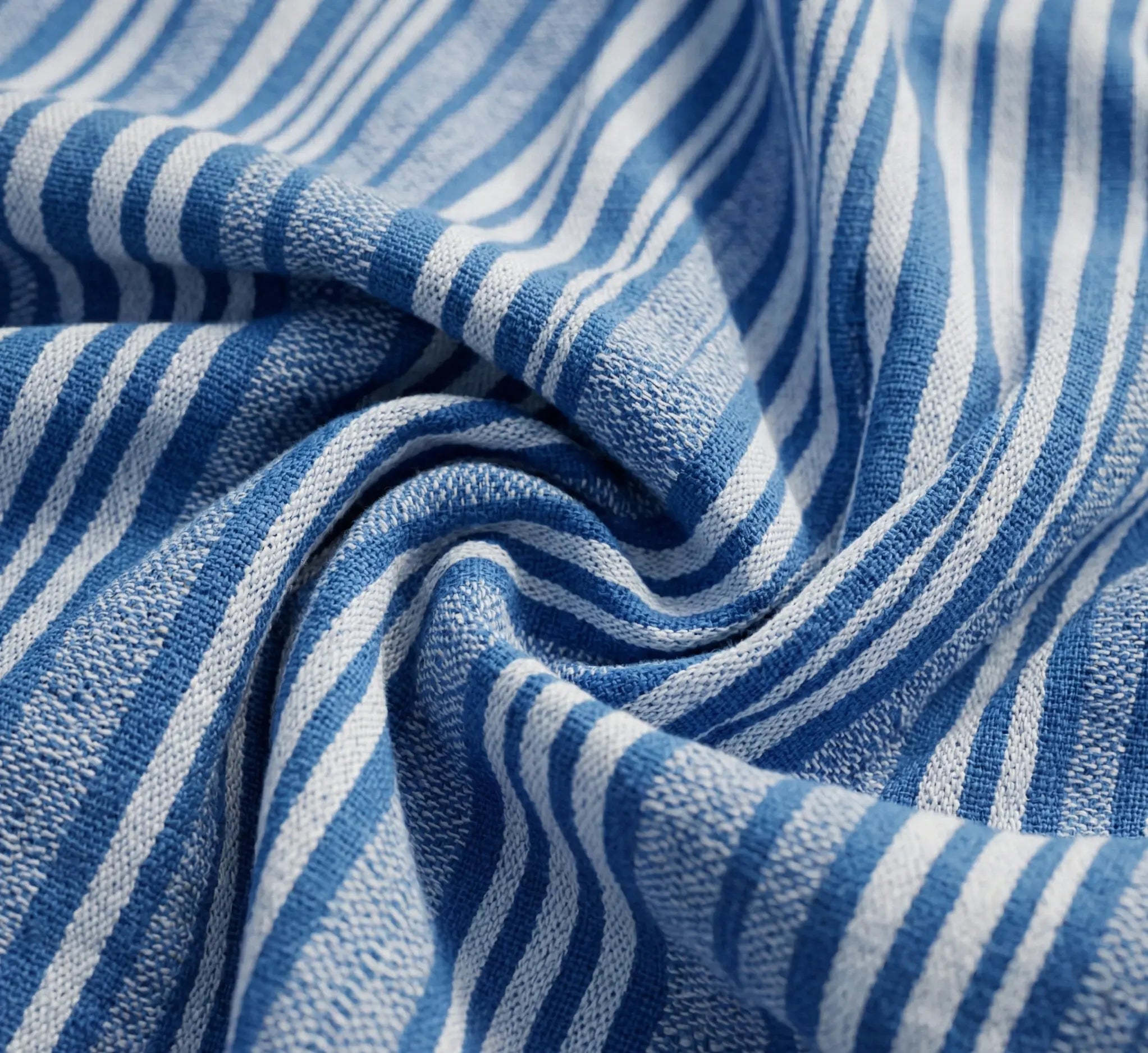 Chaise hamac en toile à rayures bleues et blanches suspendue à un support métallique noir en arc dans un jardin verdoyant et fleuri avec vue sur l'horizon ensoleillé