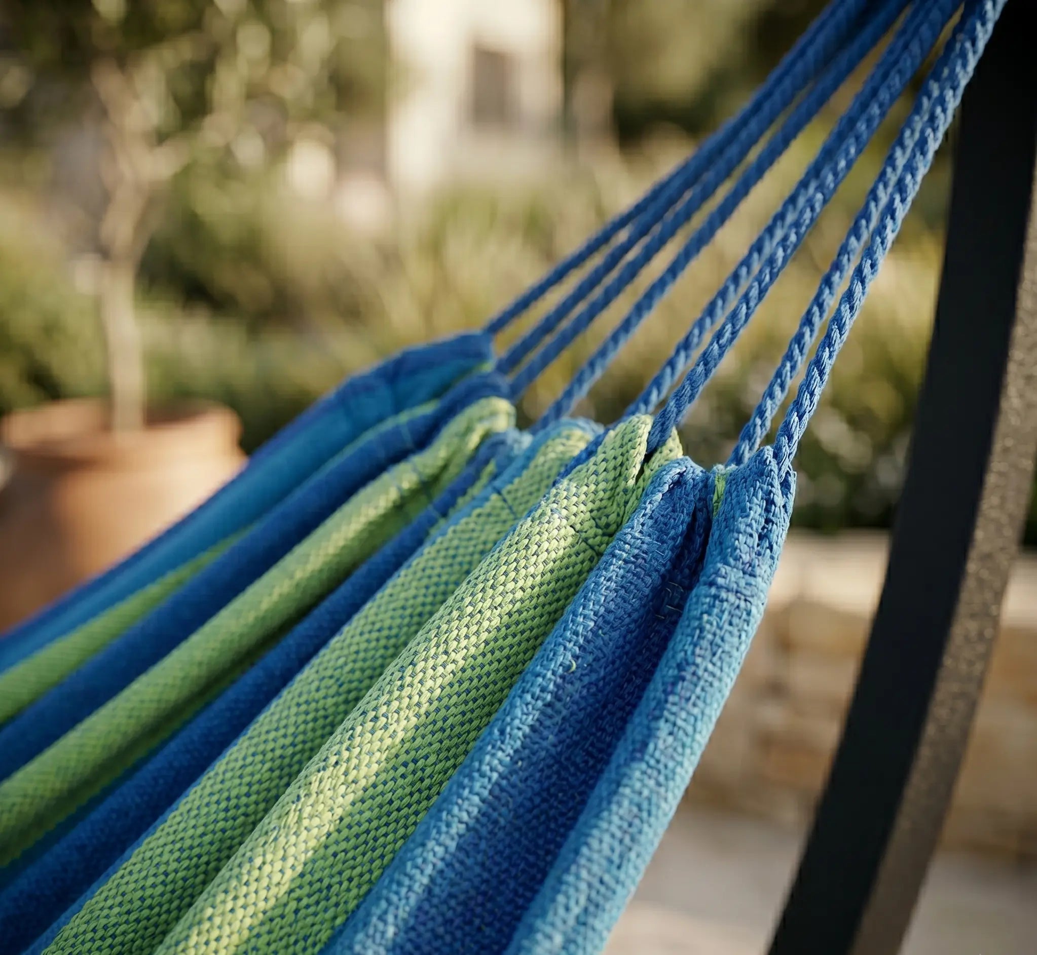 Zoom sur les cordes de suspension bleues et le tissage en coton épais d'un hamac bleu et vert citron, montrant la solidité des finitions en situation extérieure ensoleillée.