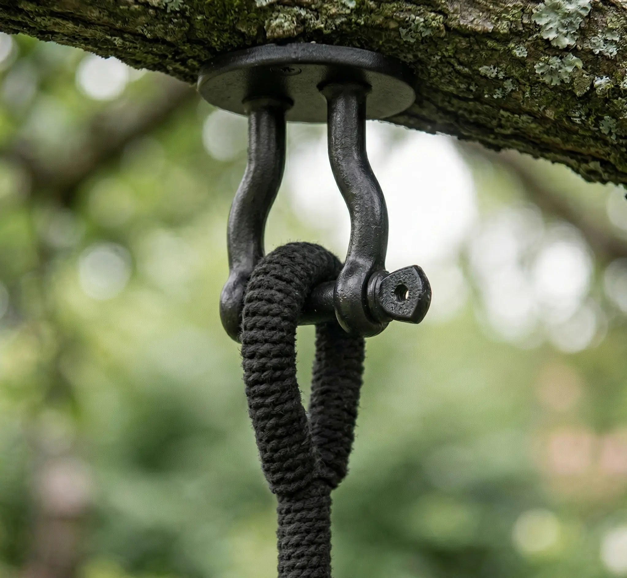 Balancelle ronde en macramé noir avec franges artisanales suspendue sur une terrasse en bois moderne avec garde-corps en verre et vue sur un jardin verdoyant