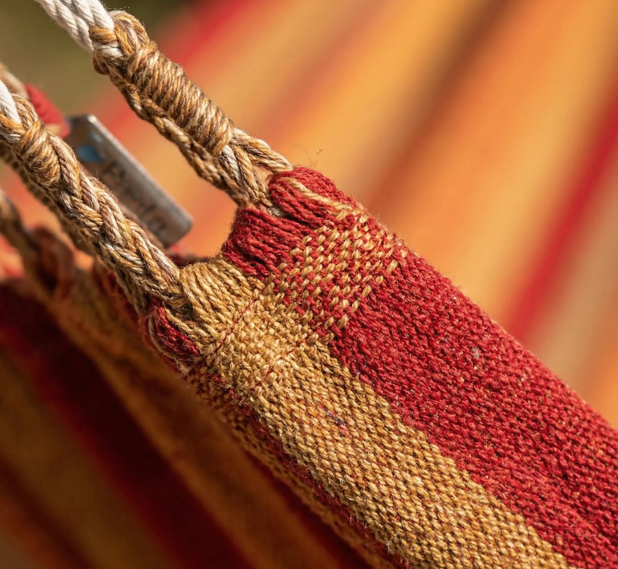 Zoom macro sur les finitions renforcées d'une toile de hamac haut de gamme montrant le tissage jacquard dense en coton terracotta et les boucles de suspension tressées à la main.
