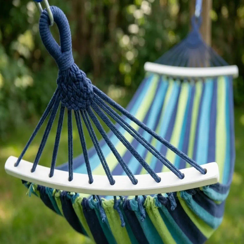 Mise en situation d'un hamac de jardin XL aux rayures bleu et vert, suspendu entre un arbre robuste et un support en bois dans un jardin ensoleillé, avec vue sur la campagne.