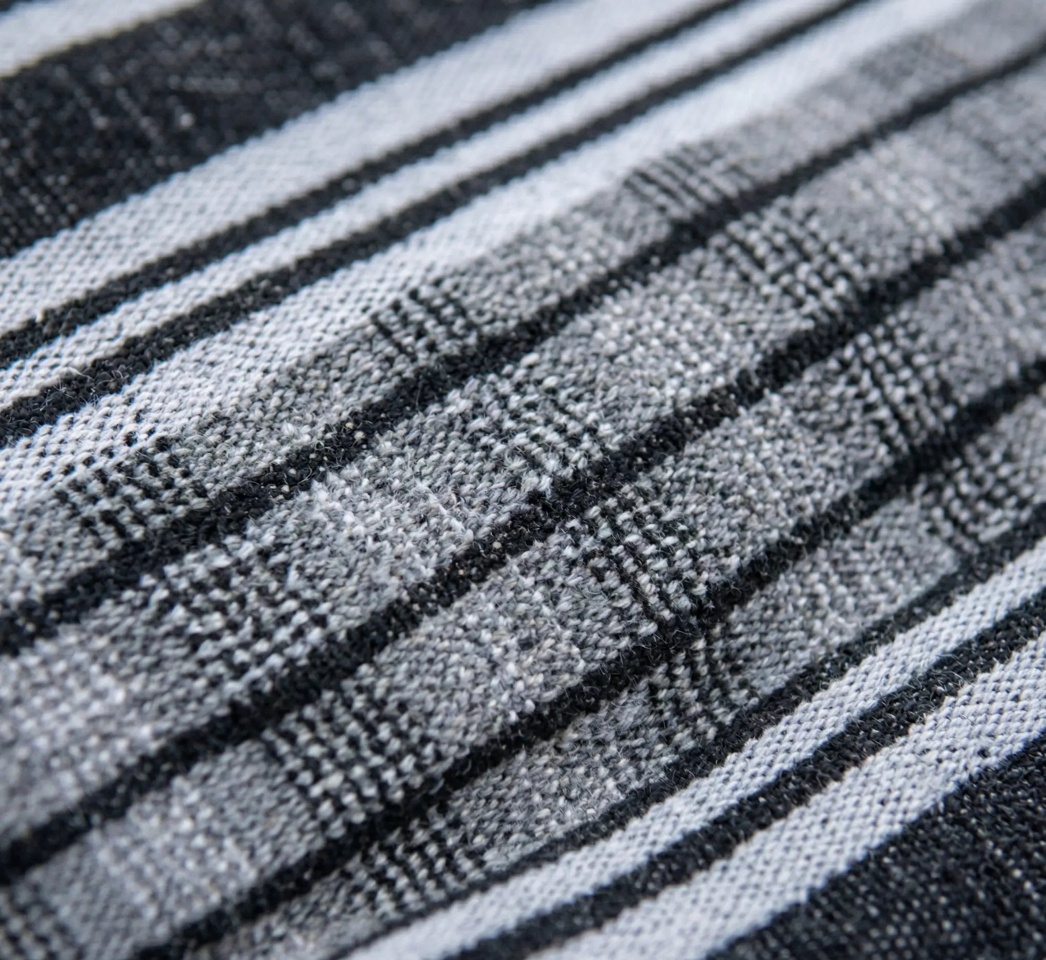 Vue macro haute résolution du tissage d'une toile de hamac en coton premium montrant l'entrelacement serré des fibres gris anthracite, gris chiné et blanc de haute densité