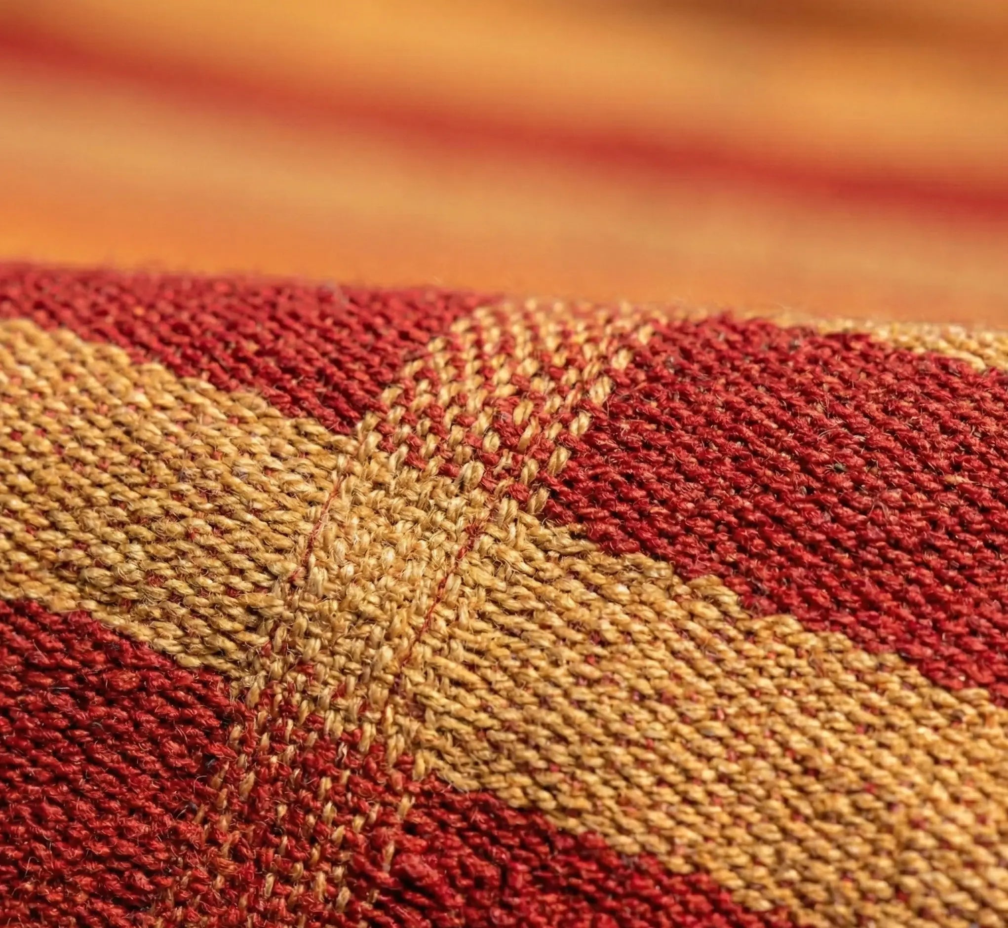 Vue macro haute précision du grain de tissage d'un hamac en coton naturel montrant l'entrelacement dense des fibres aux coloris rouge terracotta et ocre jaune.