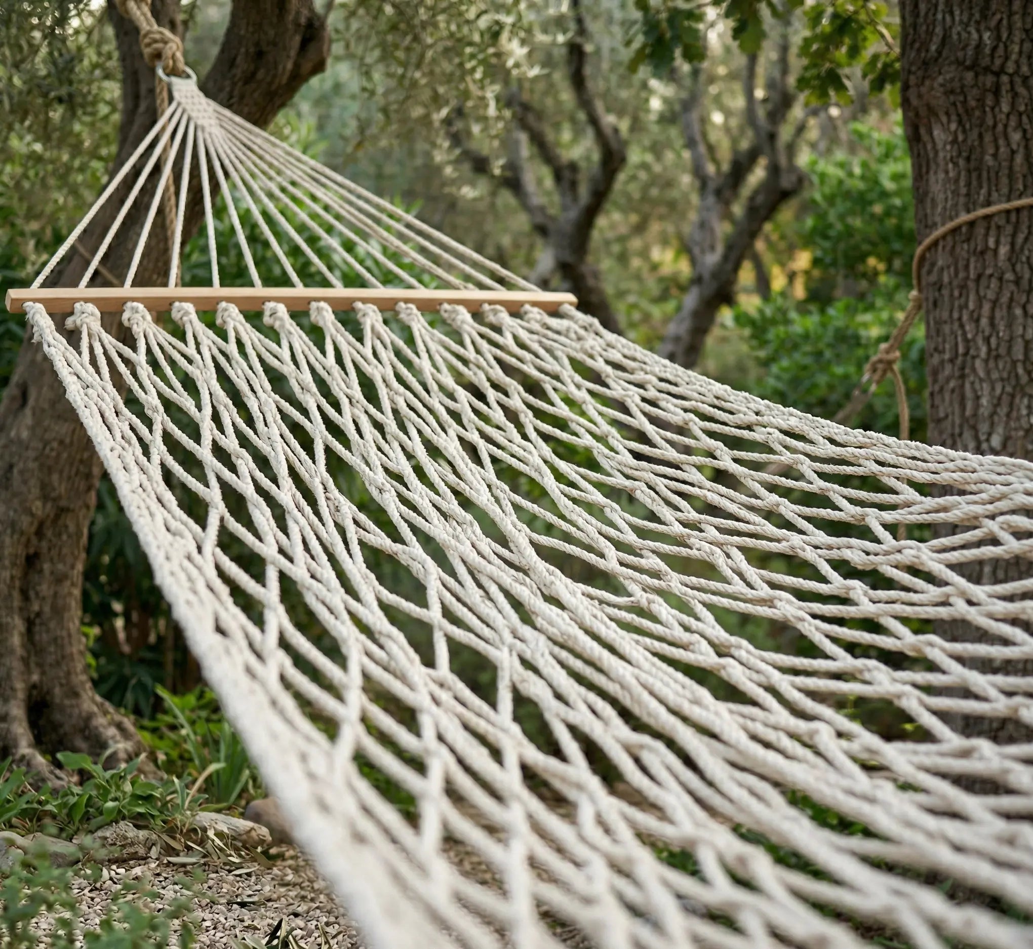 Vue en perspective d'un hamac filet à barres montrant le maillage serré en coton naturel et la barre d'écartement en bois massif sous la lumière du soleil.