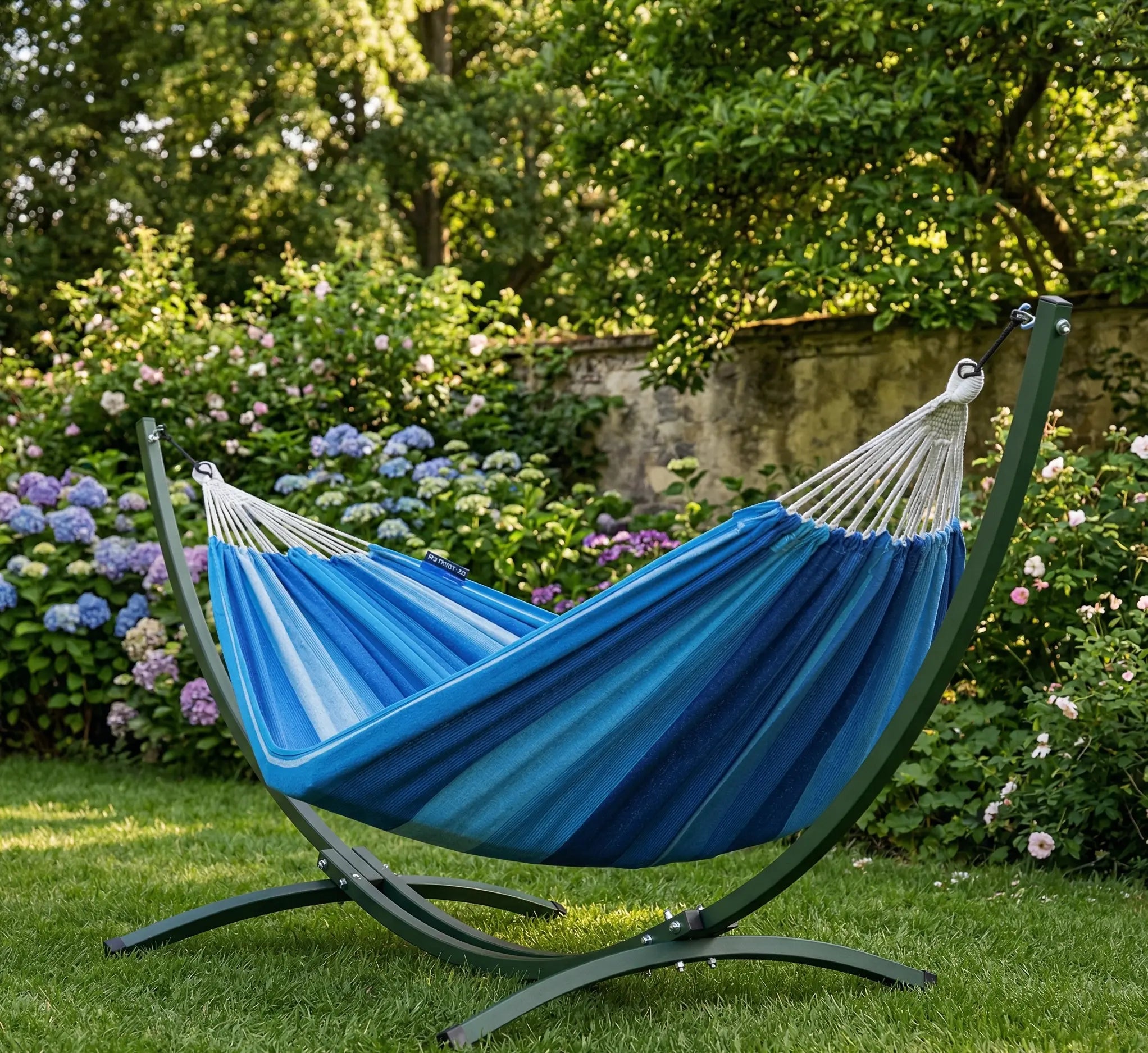 Vue de profil d'un hamac complet avec support courbé en arc acier vert forêt et une large toile en coton haute densité aux rayures dégradées bleu lagon et turquoise, sur fond blanc épuré
