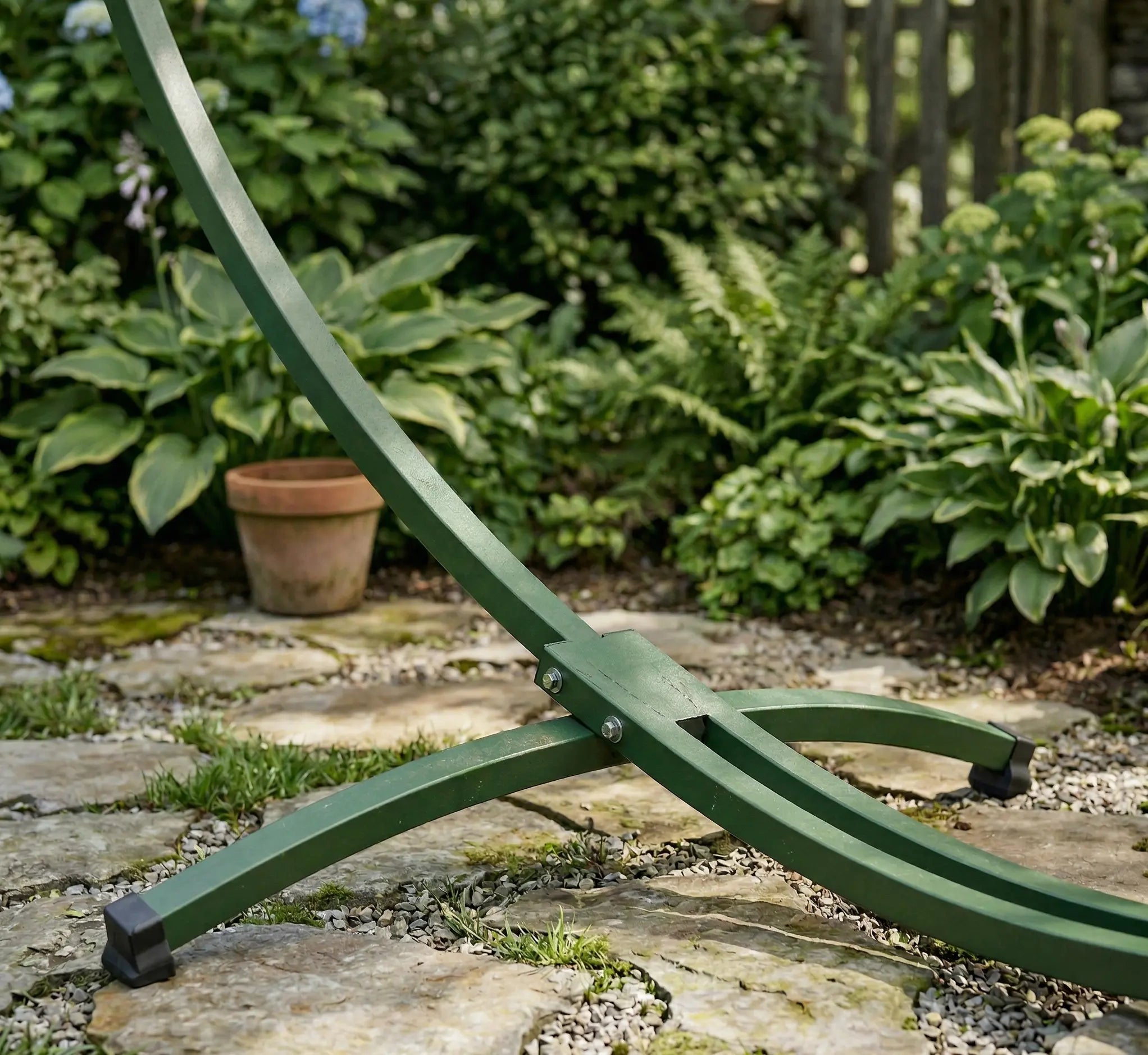 Vue détaillée du pied stabilisateur d'un support de hamac en acier vert forêt installé sur une terrasse en dalles de pierre avec patins de protection antidérapants