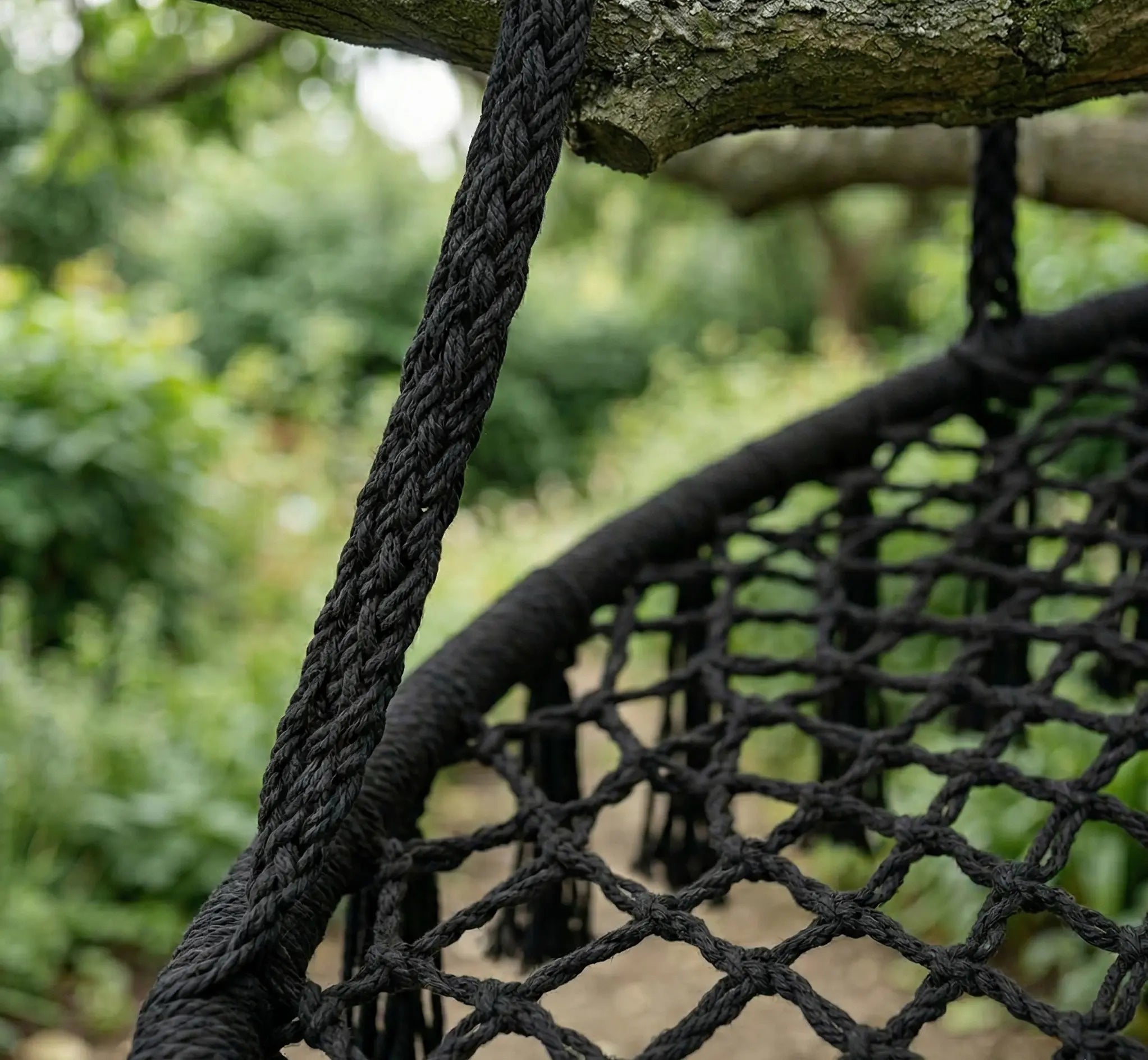 Détail d'une corde en macramé noir tressé fixée solidement à une branche d'arbre pour suspendre un fauteuil balancelle dans un jardin ombragé