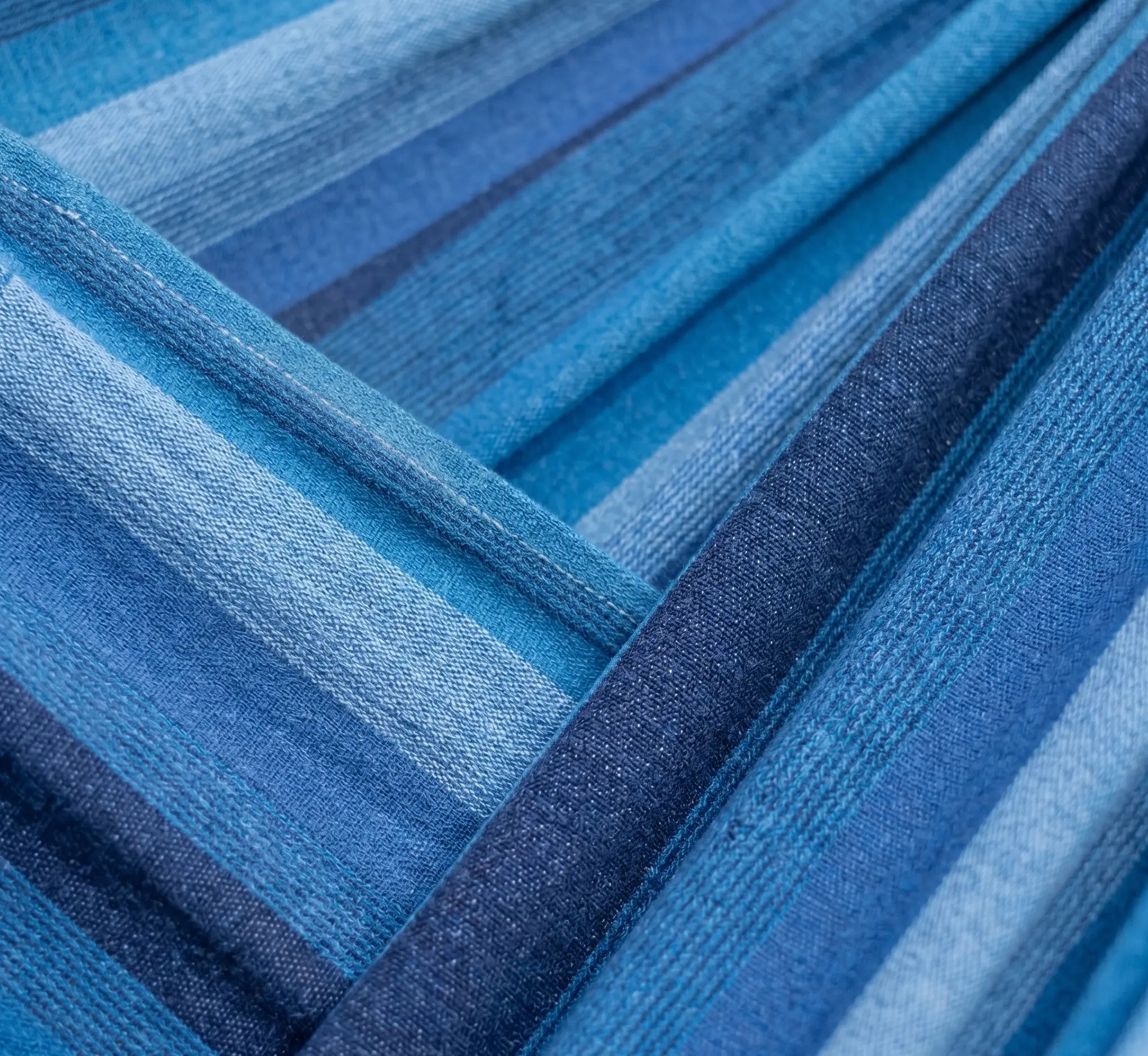 Très gros plan sur le tissage d'un hamac en coton aux différentes nuances de bleu, montrant les détails des fibres et les coutures renforcées pour un confort durable.