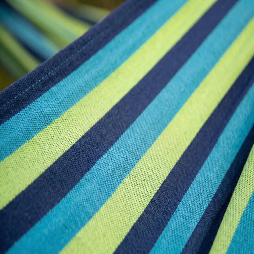 Gros plan sur le tissage serré et les coutures renforcées d'une toile de hamac en coton aux couleurs bleu marine, turquoise et vert lagon.