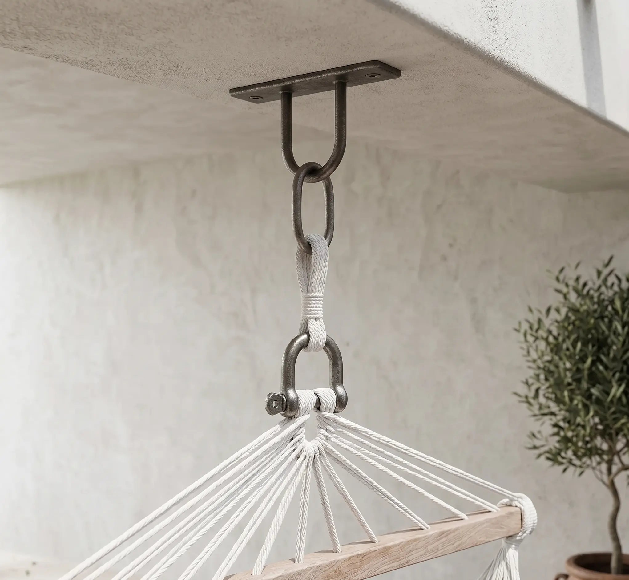 Détail d'un support de fixation en acier inoxydable ancré dans un plafond en béton, montrant la chaîne, le mousqueton de sécurité et la boucle de suspension d'un fauteuil suspendu haut de gamme.