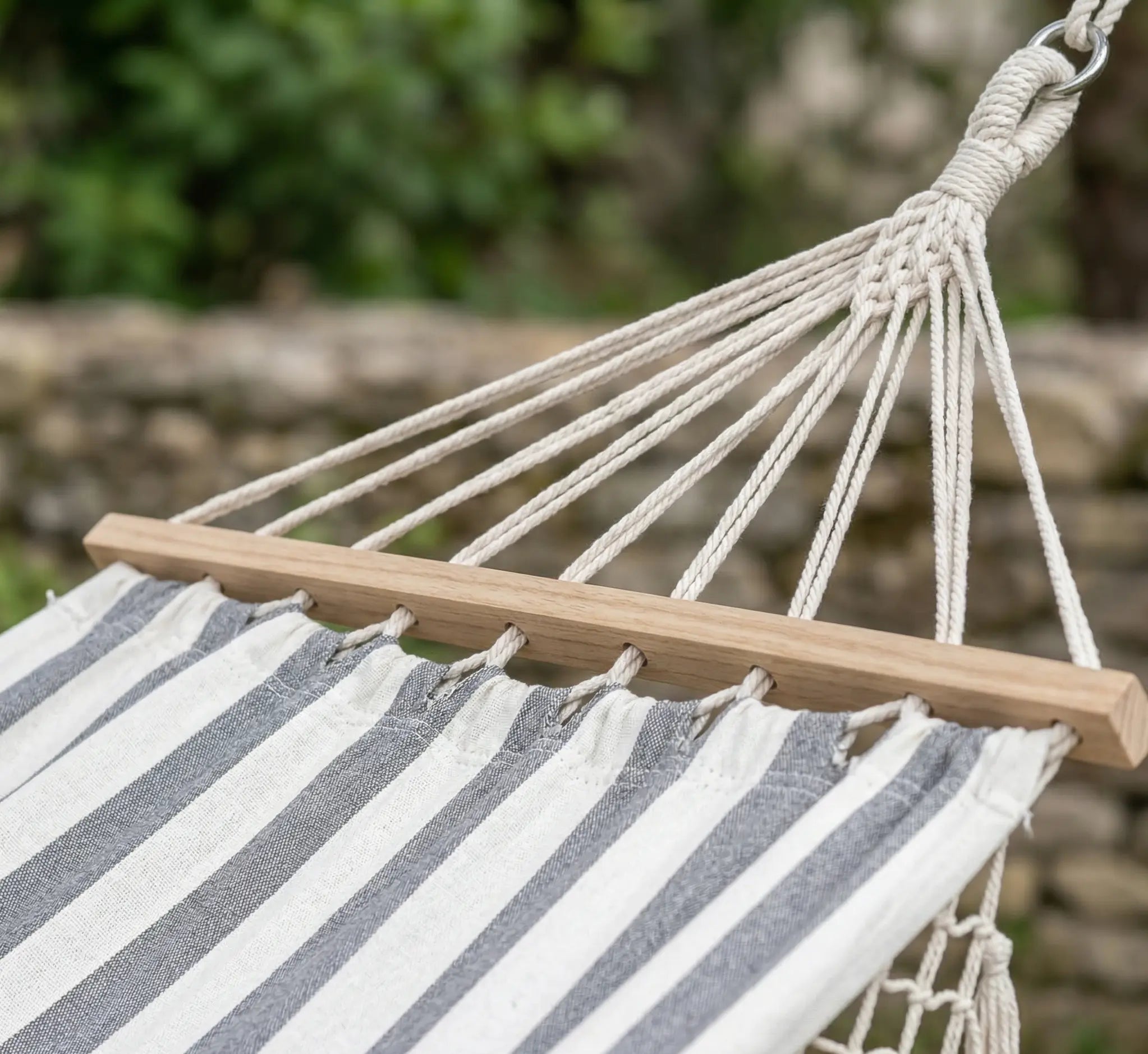 Détail de la barre d'écartement en bois de hêtre et du système de cordage robuste d'un hamac haut de gamme aux rayures gris clair et blanc.