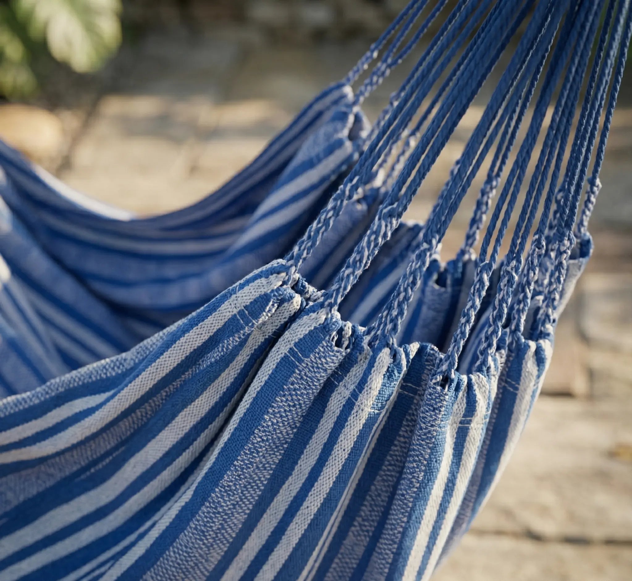 Détail rapproché des multiples cordes de suspension d'une chaise hamac à rayures bleues et blanches, montrant les finitions du tissage et la robustesse de l'attache