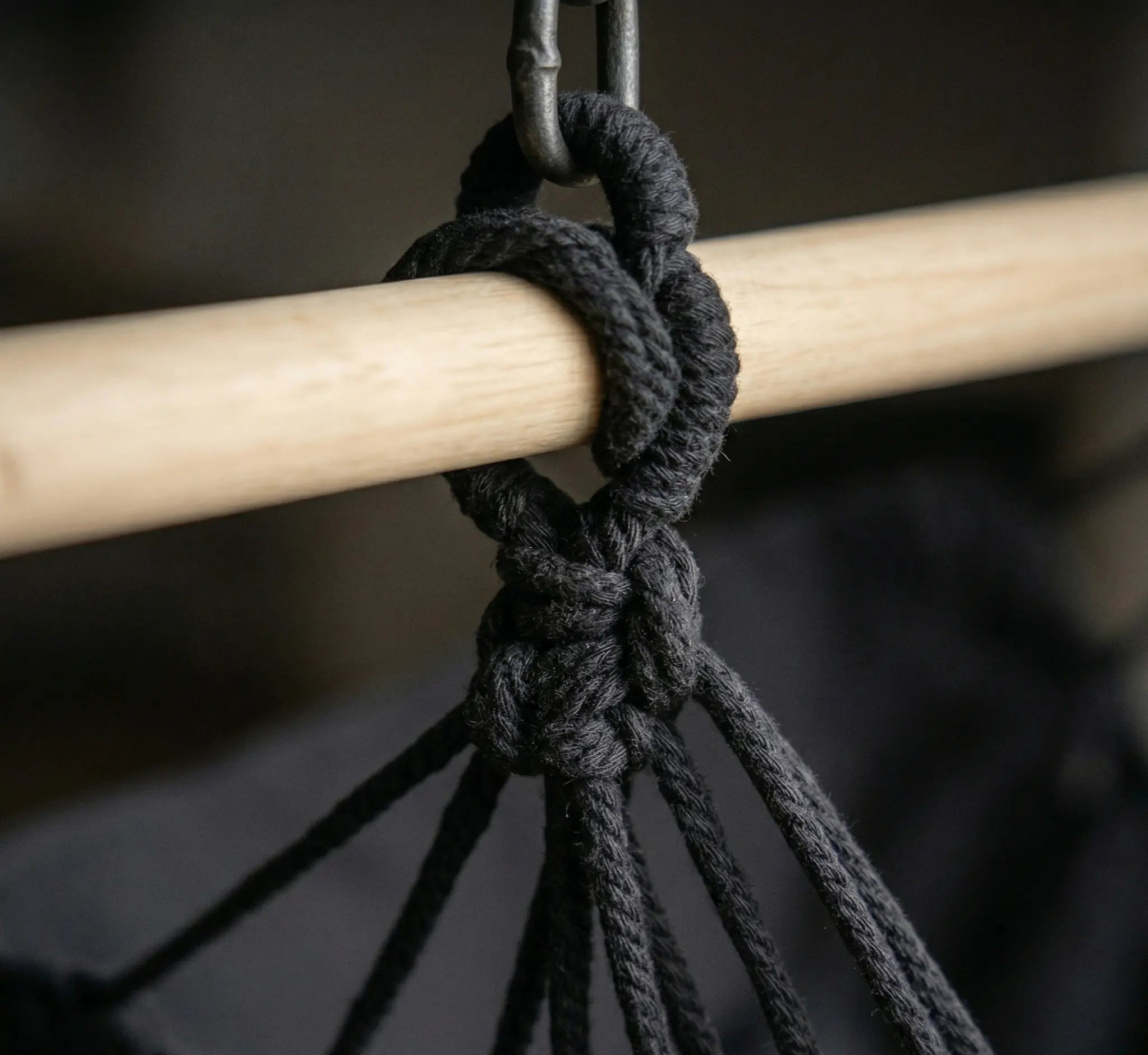 Détail rapproché du système d'attache d'une chaise hamac noire avec barre d'écartement en bois clair, nœud de suspension renforcé et maillon de chaîne en acier robuste