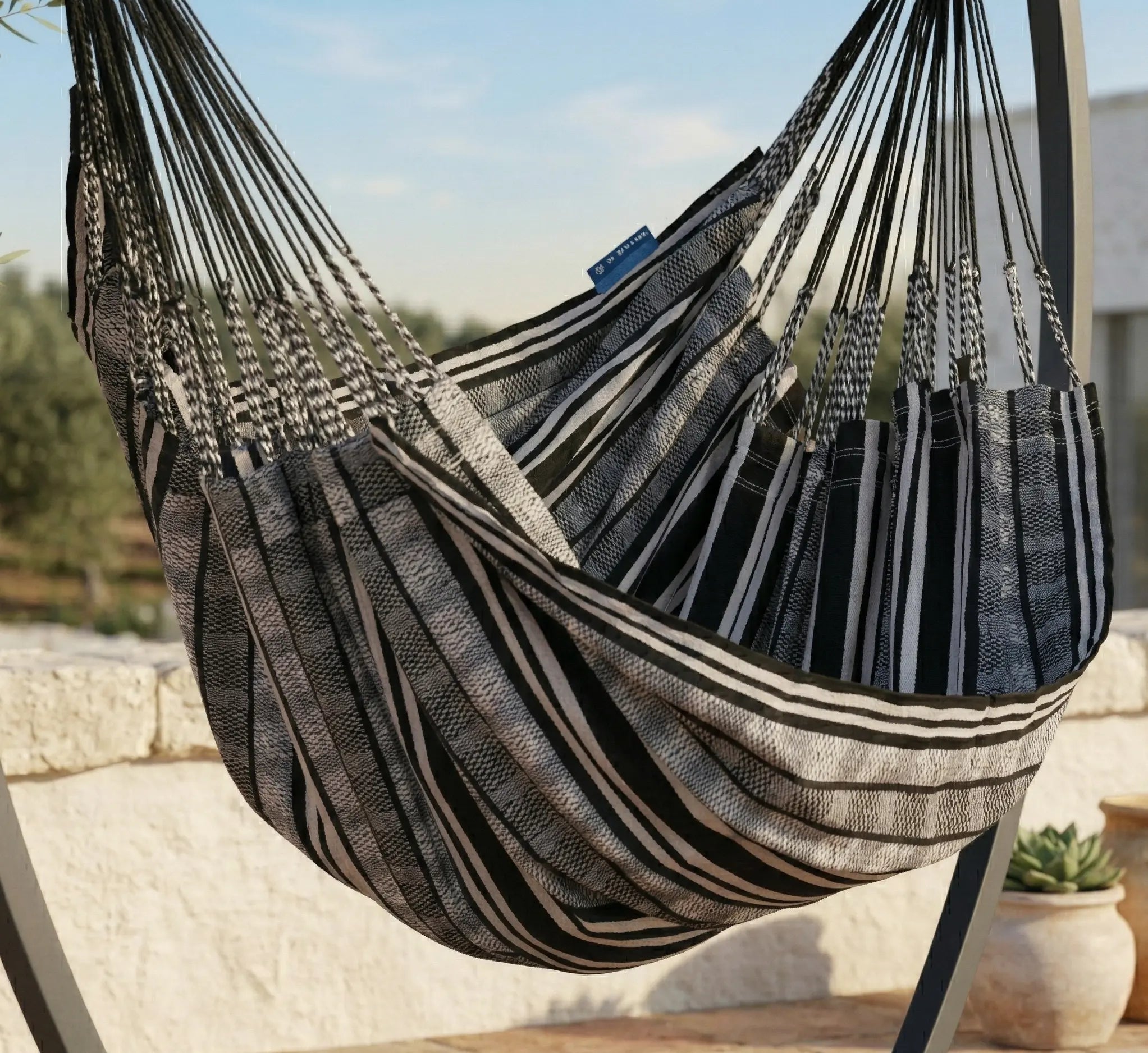 Détail rapproché d'une chaise hamac en toile à rayures noires et grises montrant les nombreuses cordes de suspension tressées et la texture robuste du tissu sur une terrasse ensoleillée