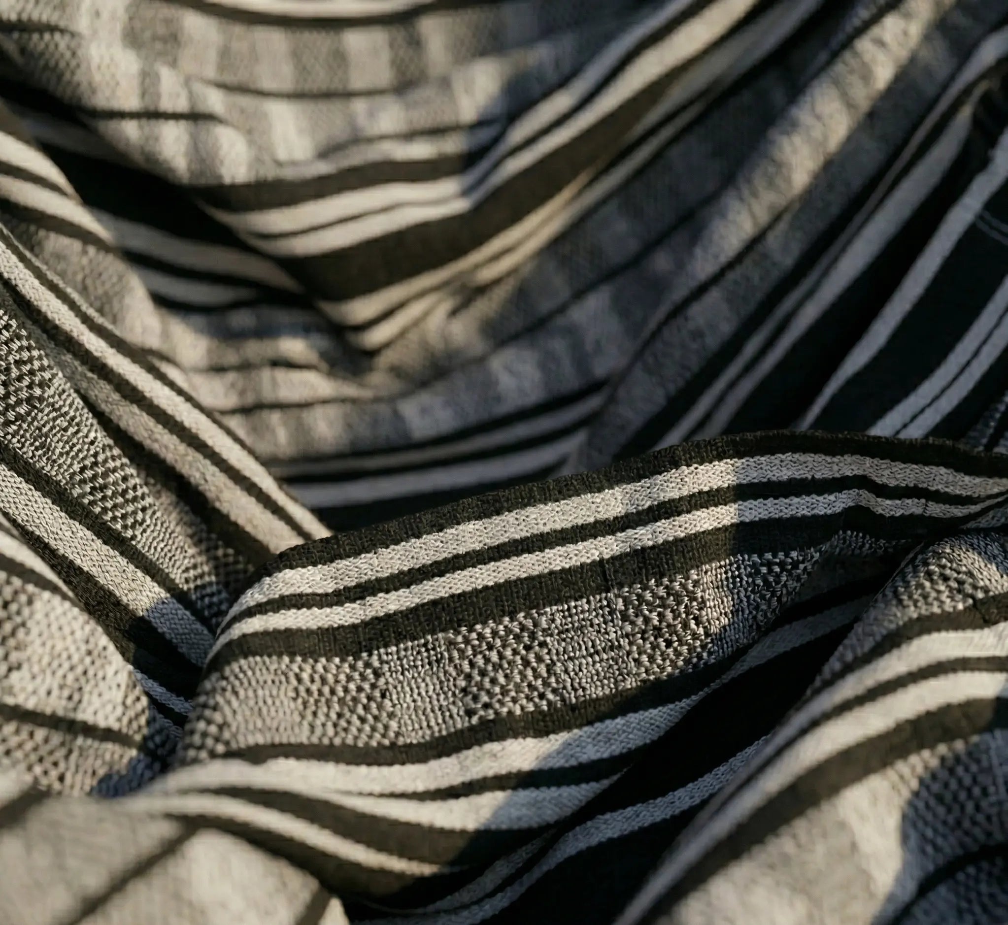 Gros plan sur le tissage serré d'une toile de hamac à rayures noires et grises, montrant la texture du coton renforcé et la densité des fibres pour une haute résistance