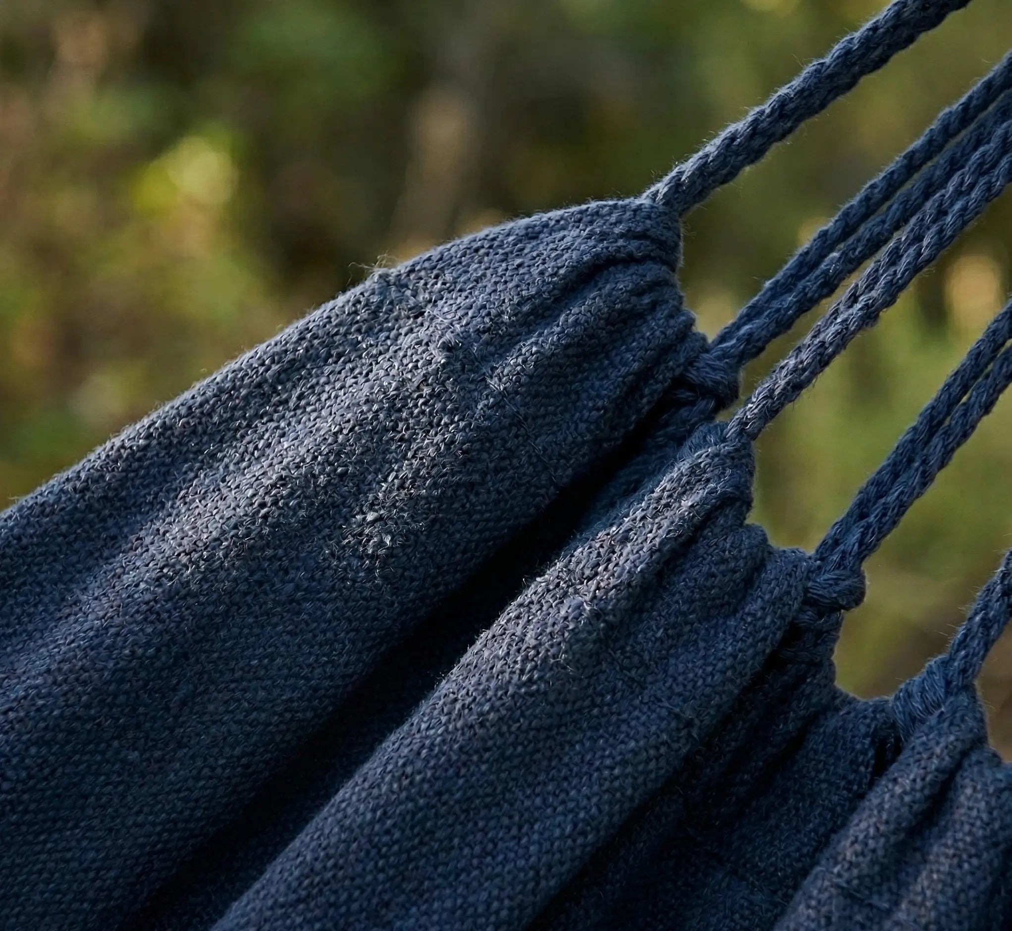 Gros plan sur les coutures renforcées et les cordes de suspension tressées d'un hamac en coton bleu marine premium illustrant la durabilité des finitions