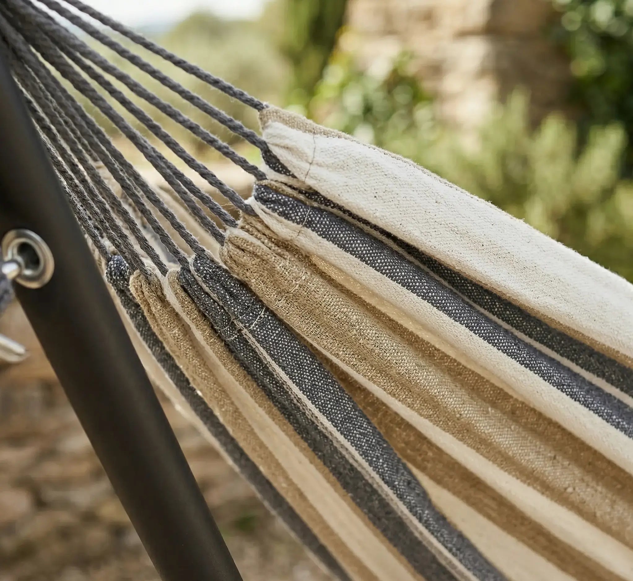 Zoom sur les suspentes renforcées et le tissage en coton naturel d'un hamac de luxe aux tons beige sable et gris anthracite installé sur un support en acier noir