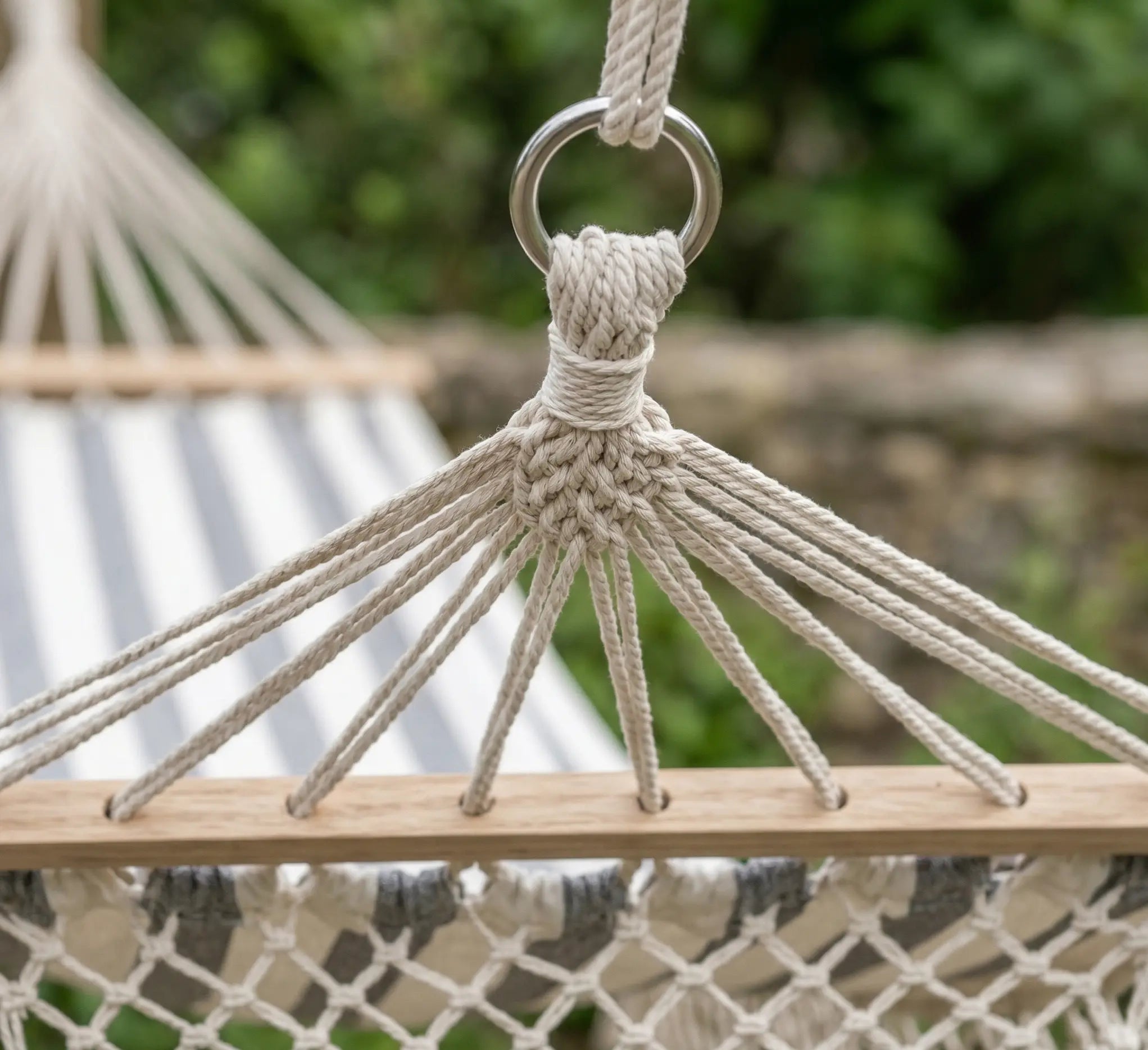 Gros plan sur les franges délicates en macramé tressées à la main et les pompons décoratifs d'un hamac de luxe à barres aux rayures gris et blanc.
