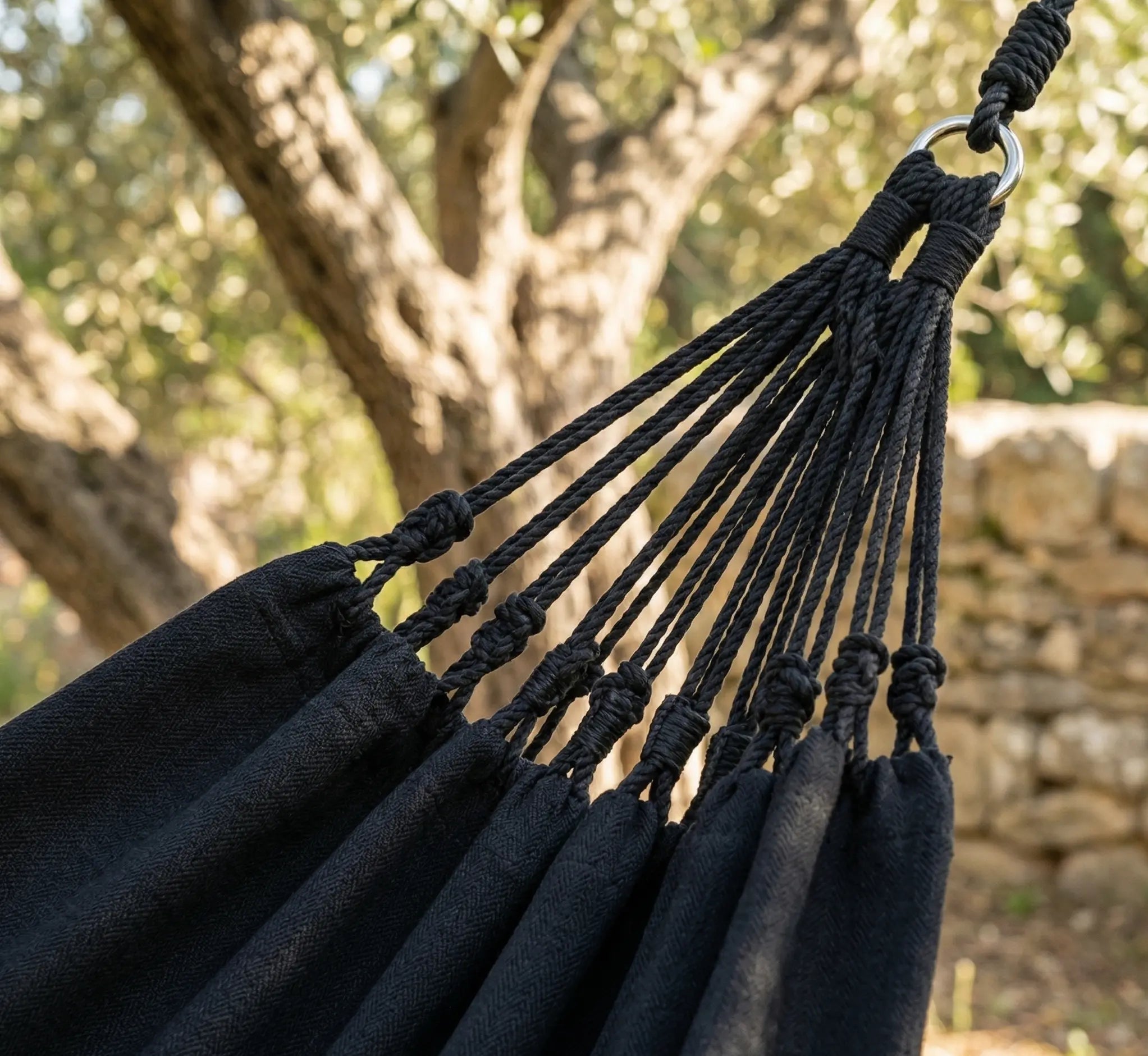Gros plan sur les franges délicates en macramé tressées à la main et les pompons décoratifs d'un hamac de luxe en coton noir intense.