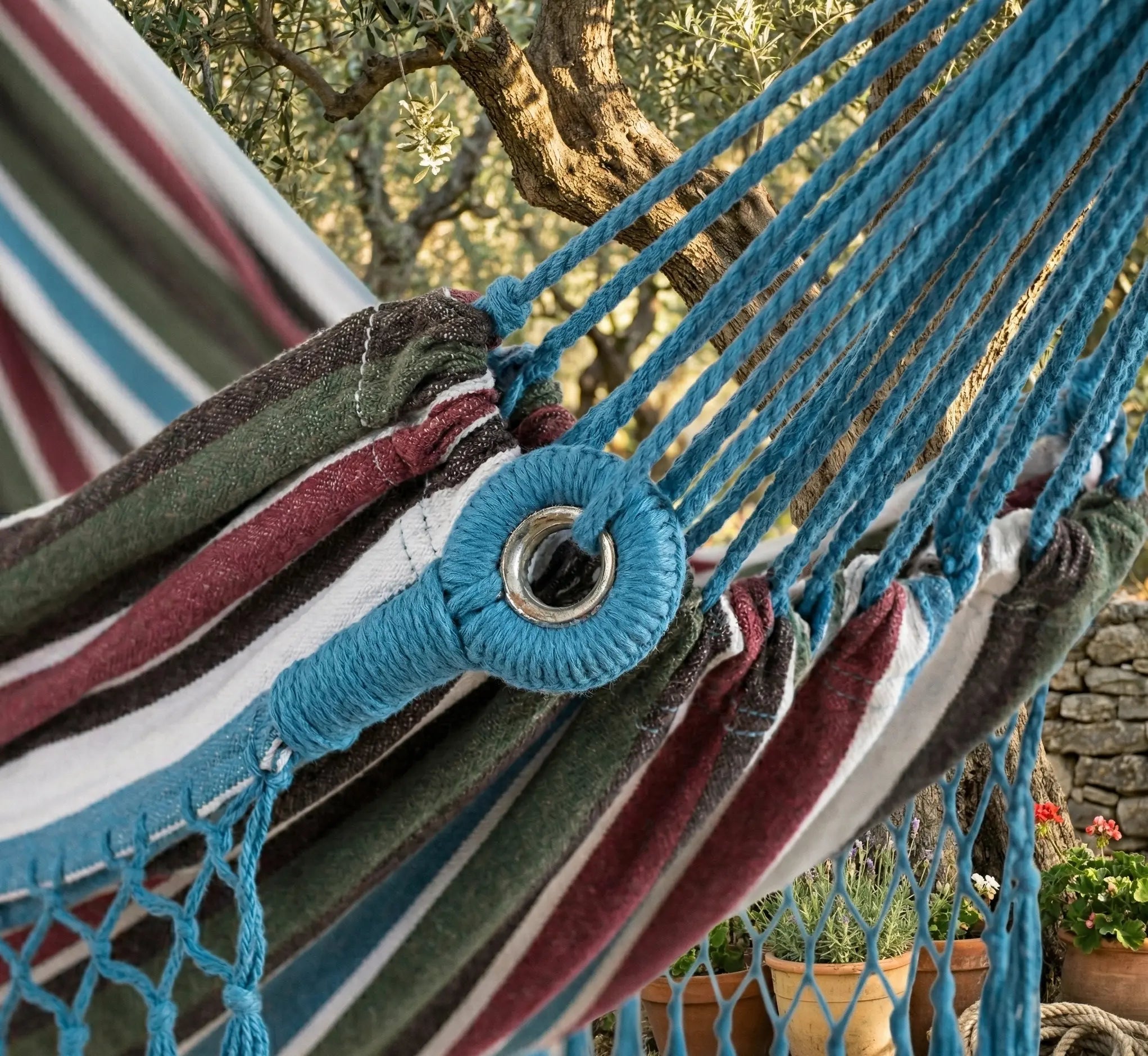 Gros plan sur l'œillet métallique de sécurité et le tressage bleu artisanal d'un hamac de luxe aux rayures bordeaux et azur.