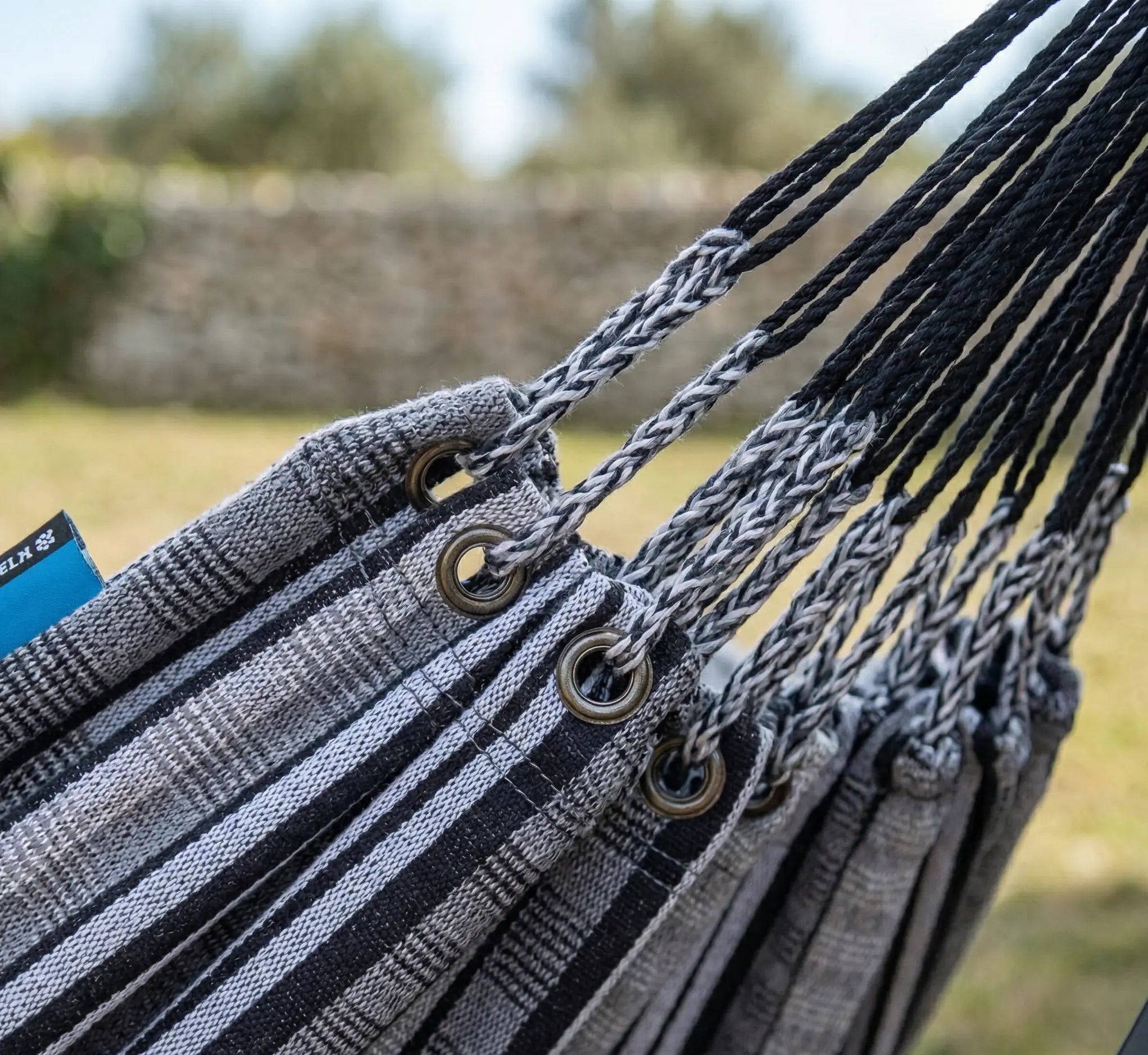 Zoom sur les œillets en acier et les suspentes tressées bicolores d'un hamac de luxe aux rayures gris anthracite et blanc pour une résistance maximale en extérieur