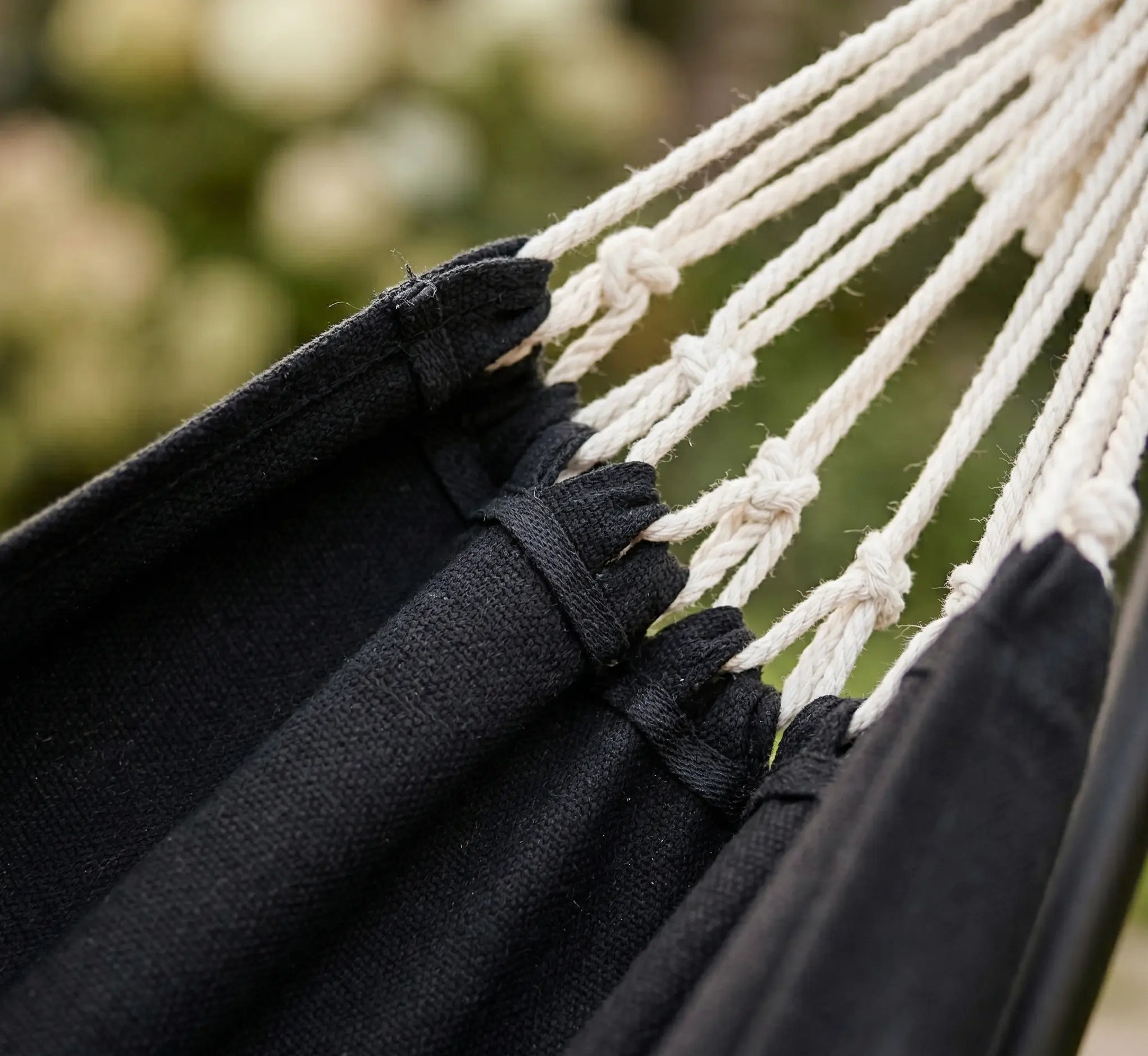 Zoom sur les attaches renforcées et les cordages en coton blanc tressé d'un hamac de luxe avec toile noire de haute densité en extérieur