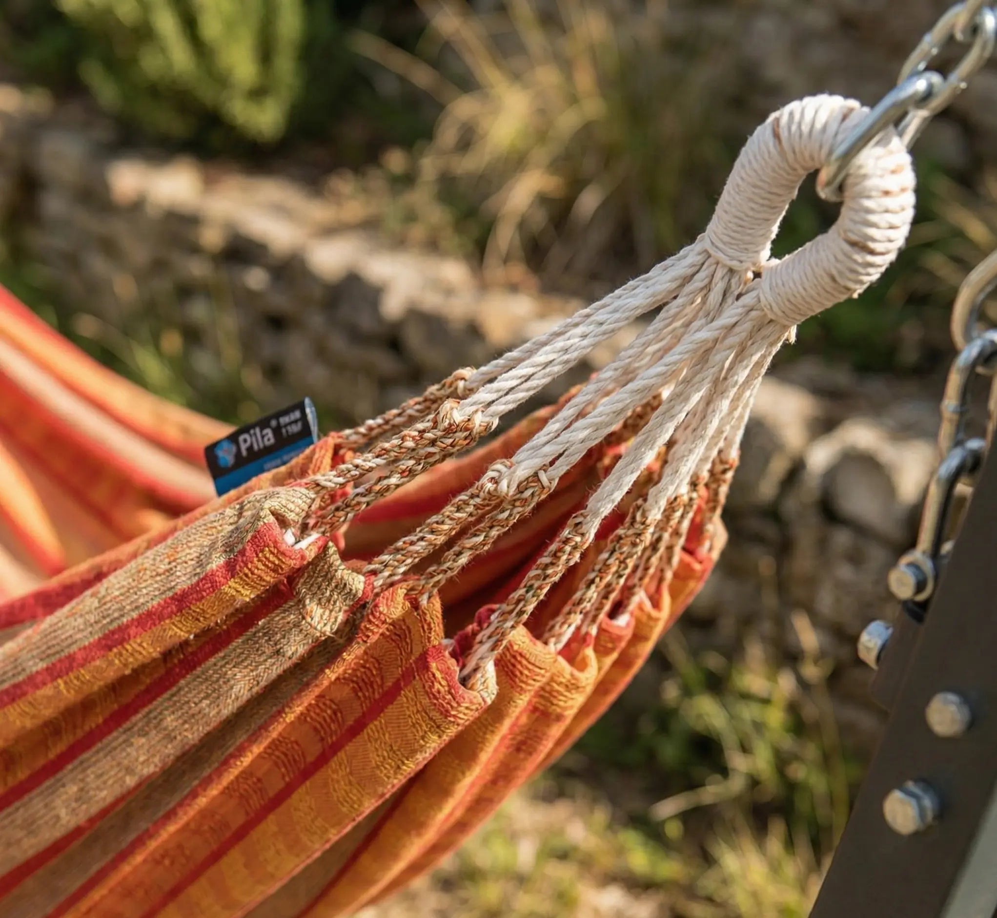 Zoom sur les boucles de suspension renforcées et les cordages tressés à la main d'un hamac de luxe aux rayures terracotta et ocre sur un support design