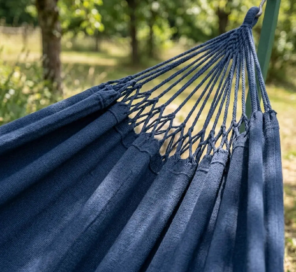 Zoom sur les suspentes en coton tressé bicolore et la toile bleu marine d'un hamac de luxe montrant la résistance des points d'attache artisanaux sur un support vert
