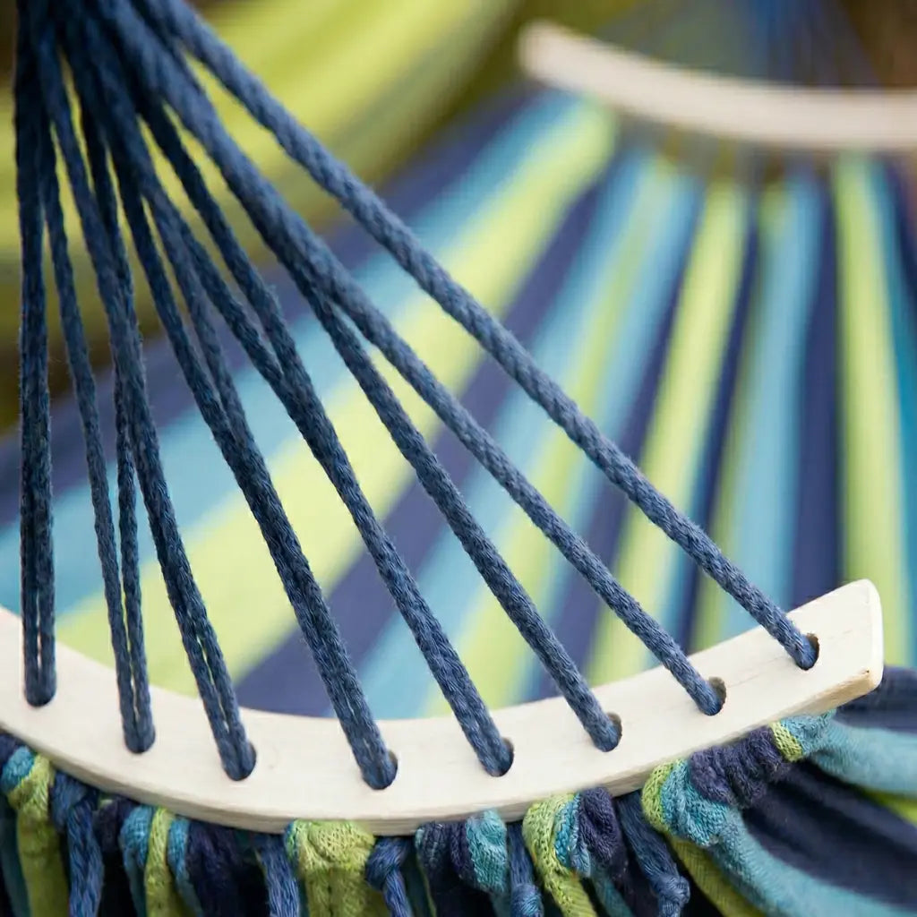 Gros plan sur le tissage en coton épais aux rayures bleu marine turquoise et vert pomme, avec les cordes de suspension tressées et la barre de bois blanche d'un hamac de jardin haut de gamme.