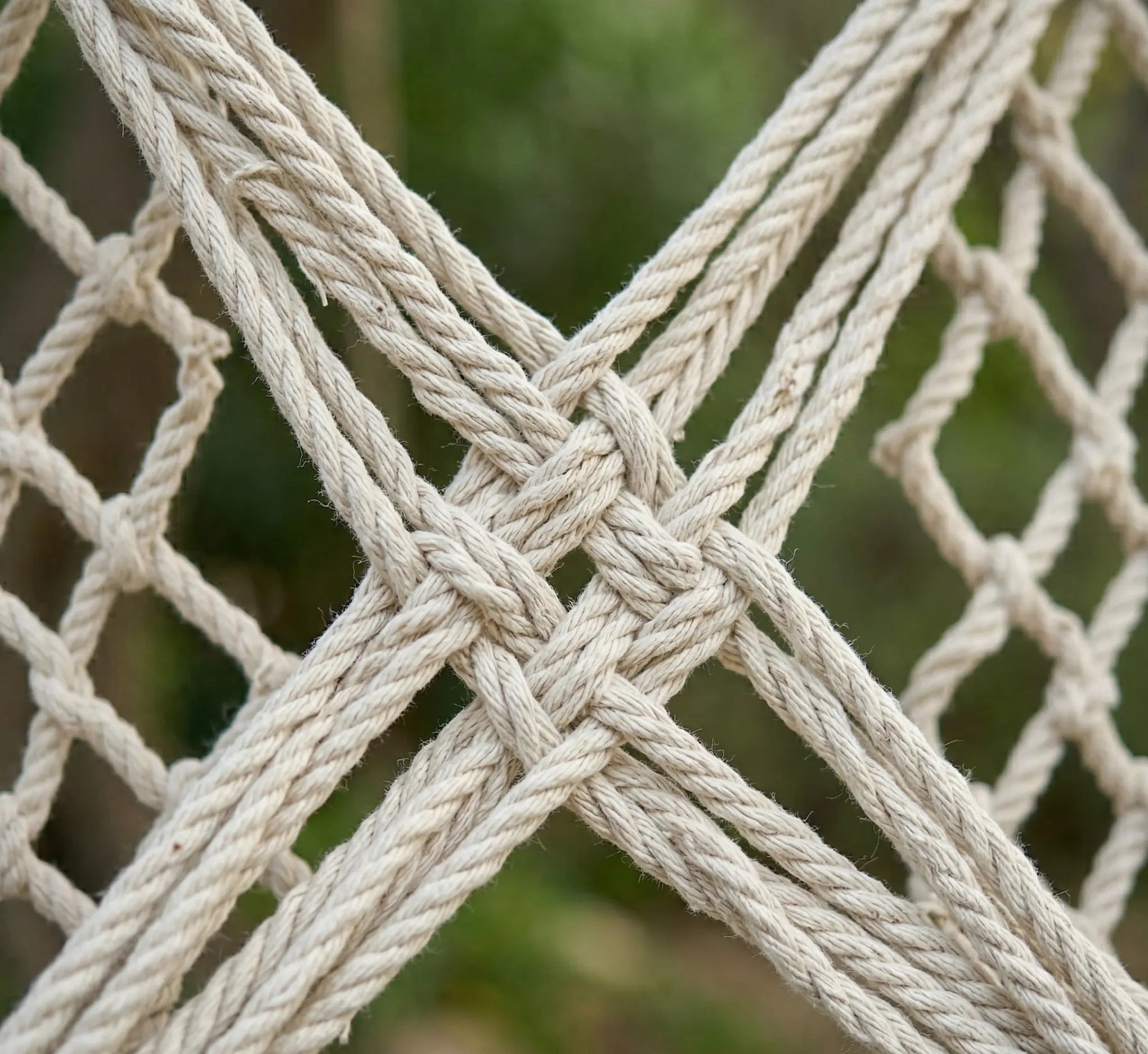 Gros plan sur les nœuds complexes et le tressage artisanal en mailles d'un hamac filet de luxe en coton écru, montrant la solidité et la qualité des finitions.