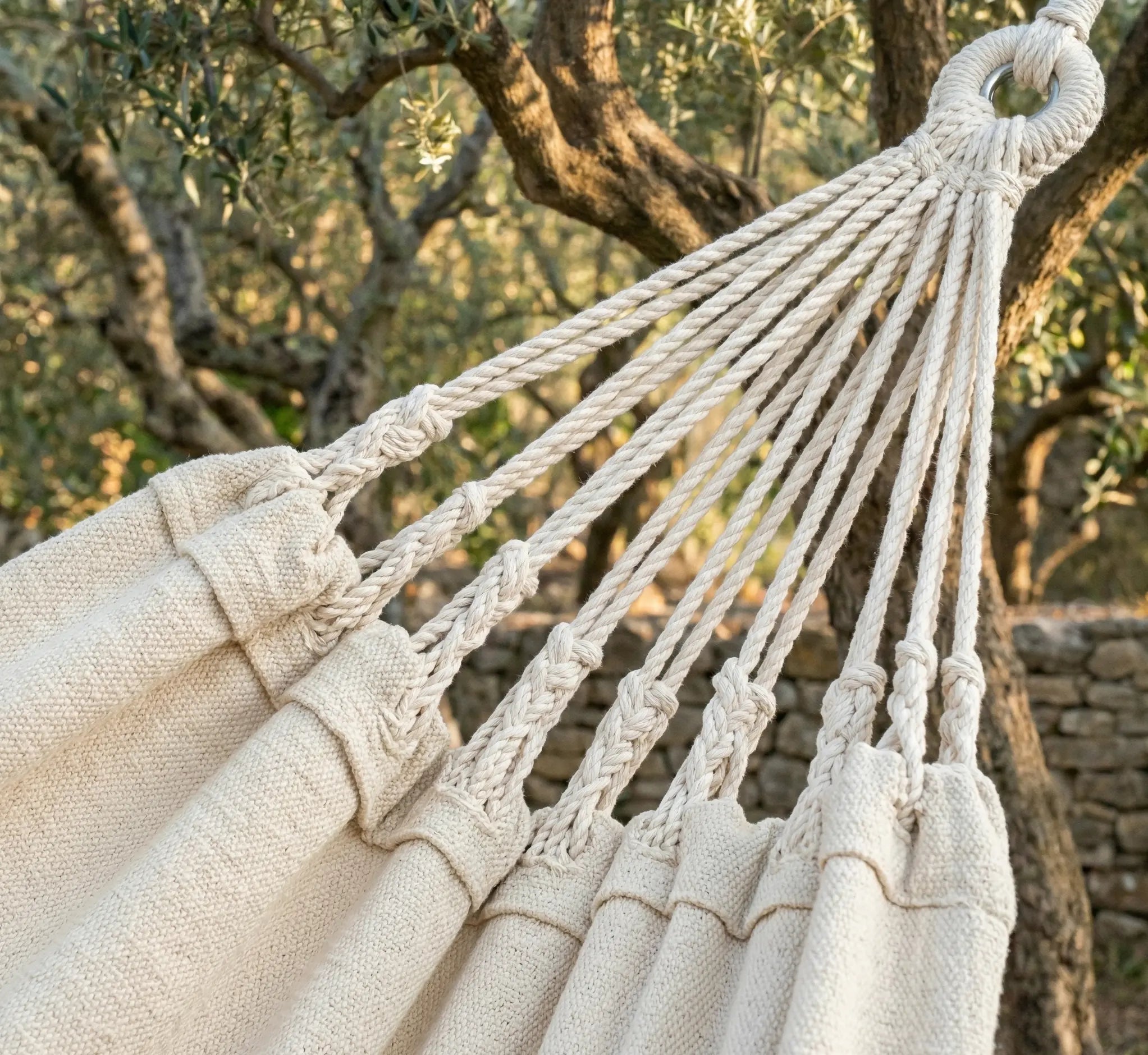 Gros plan sur les finitions artisanales et les cordes de suspension tressées à la main d'un hamac de luxe en coton écru naturel.