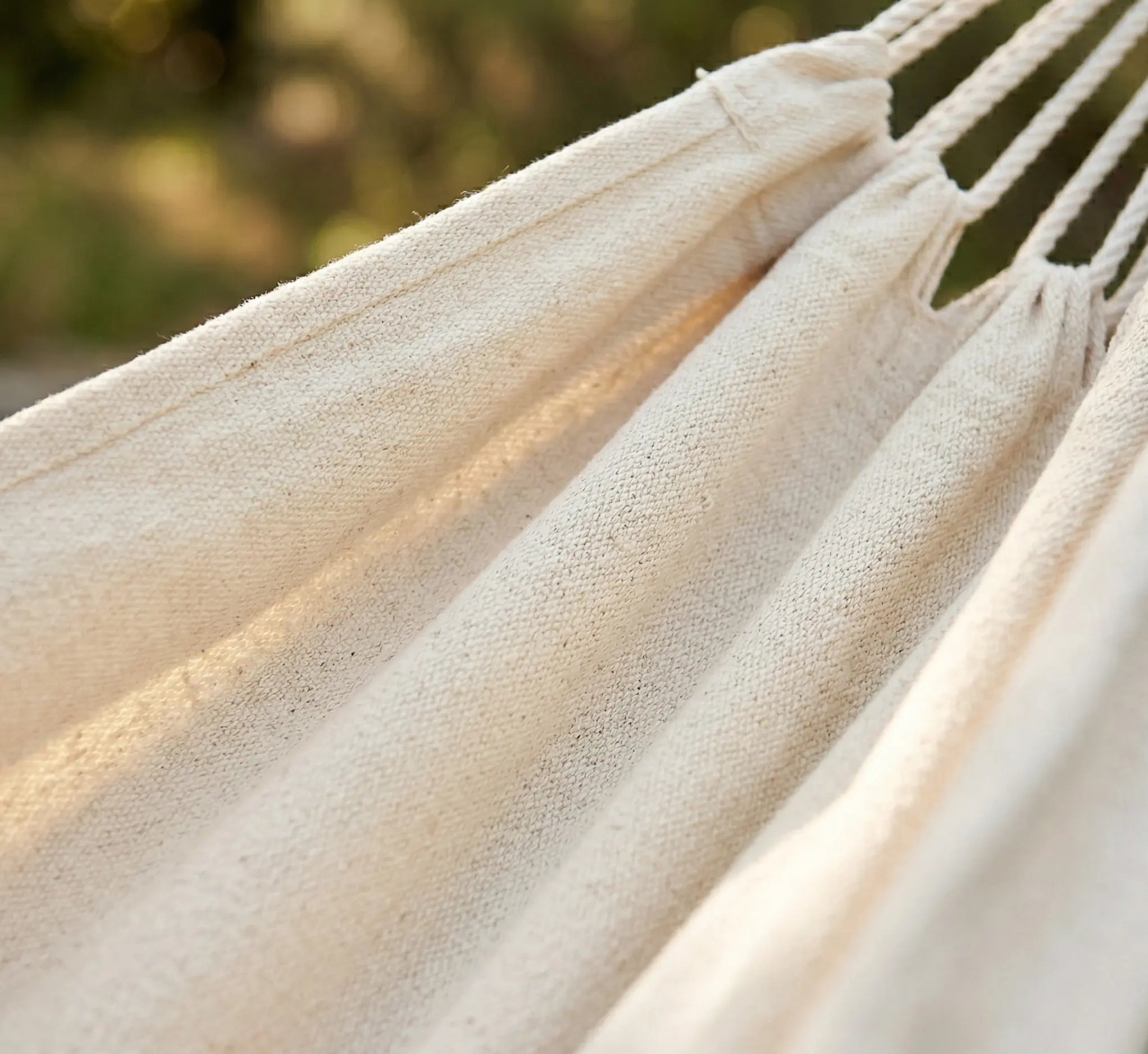Détail du tissage serré en coton naturel écru d'un hamac de luxe montrant la texture douce et respirante de la toile avec suspentes blanches en extérieur