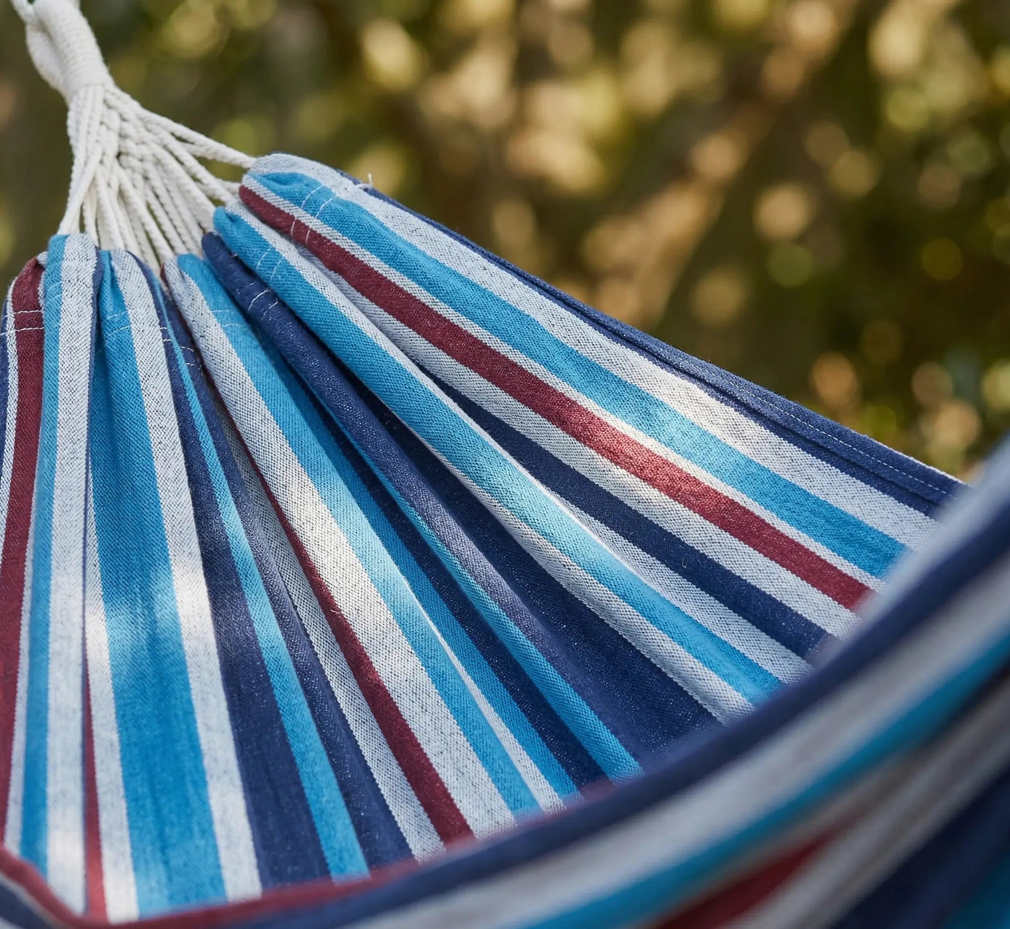 Gros plan texturé sur le tissage dense en coton naturel d'une toile de hamac haut de gamme avec rayures tricolores bleu blanc et rouge sous la lumière du soleil