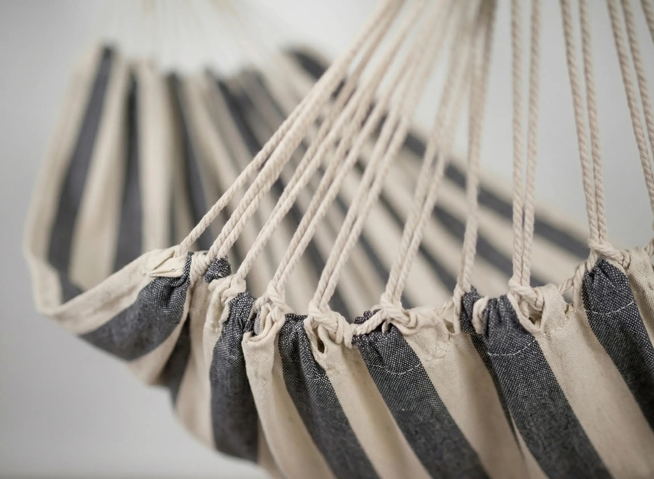 Hamac de jardin à rayures bleu et blanc sur fond blanc, équipé de barres d'écartement en bois et de boucles de fixation robustes.