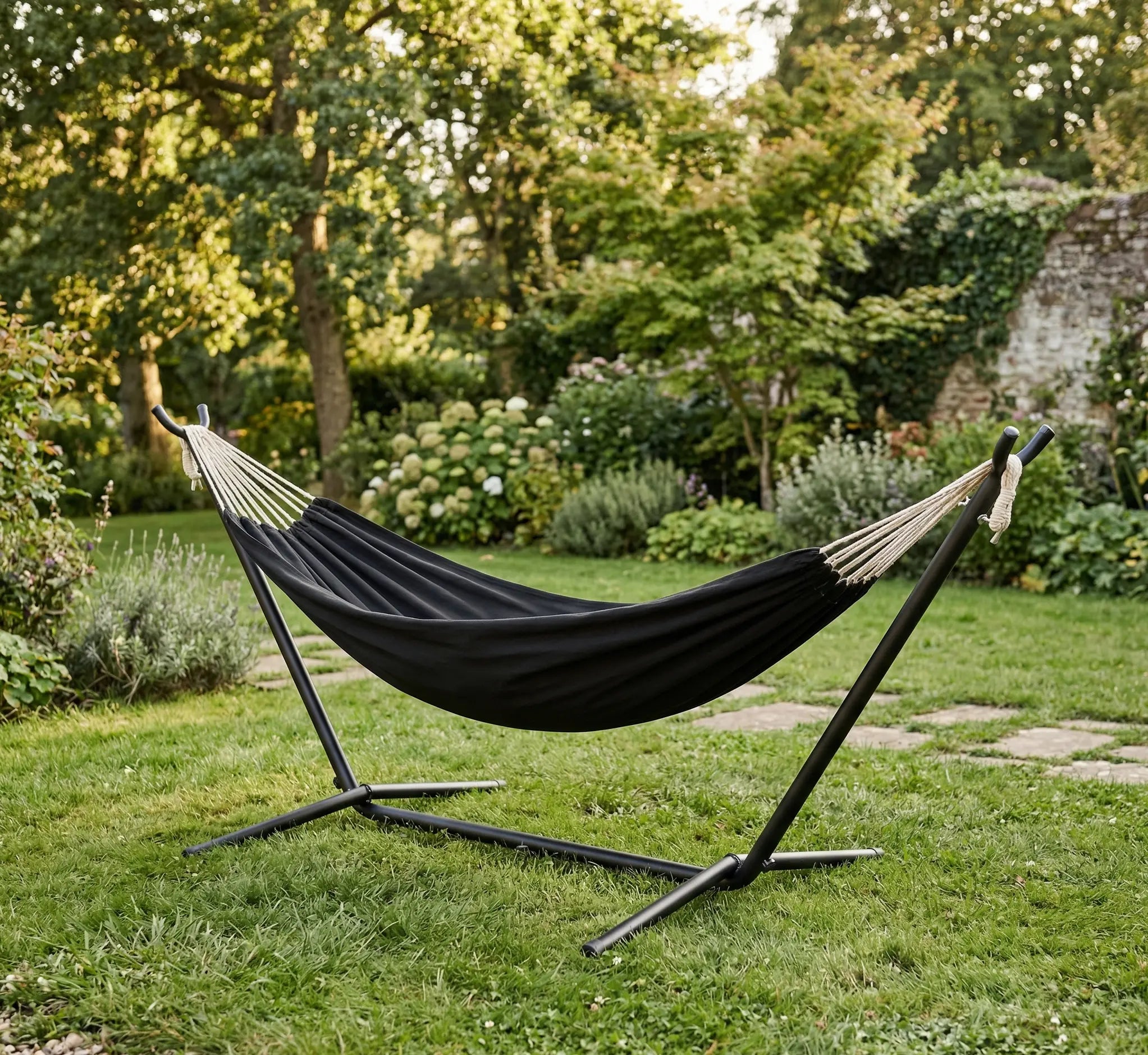 Hamac autoportant avec support en métal noir installé dans un jardin arboré, doté d'une toile en coton noir uni de haute qualité en extérieur ensoleillé