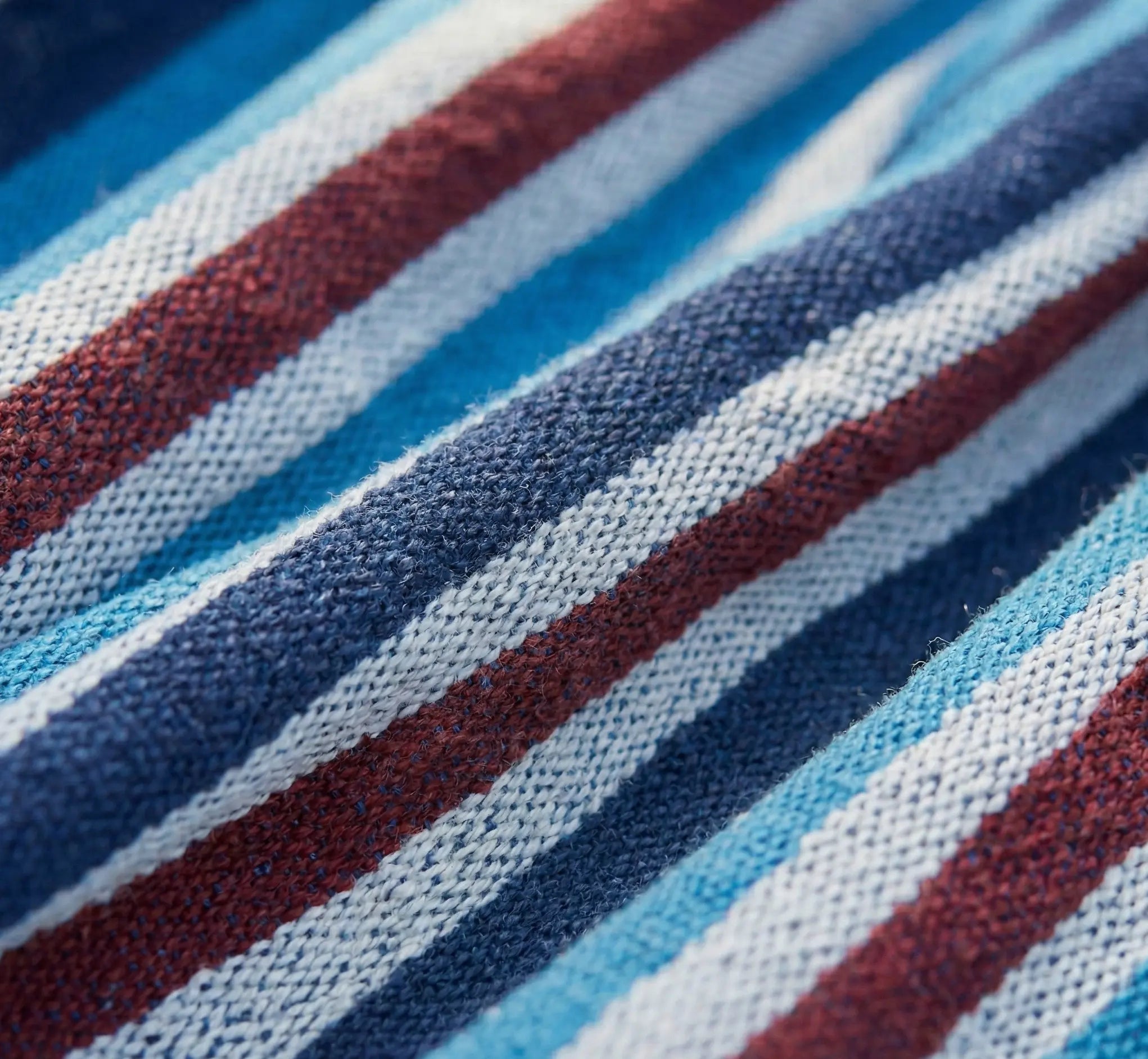 Photographie macro révélant la texture du grain et la densité exceptionnelle du tissage en coton pur d'un hamac de luxe avec rayures bleu marine bordeaux et blanc