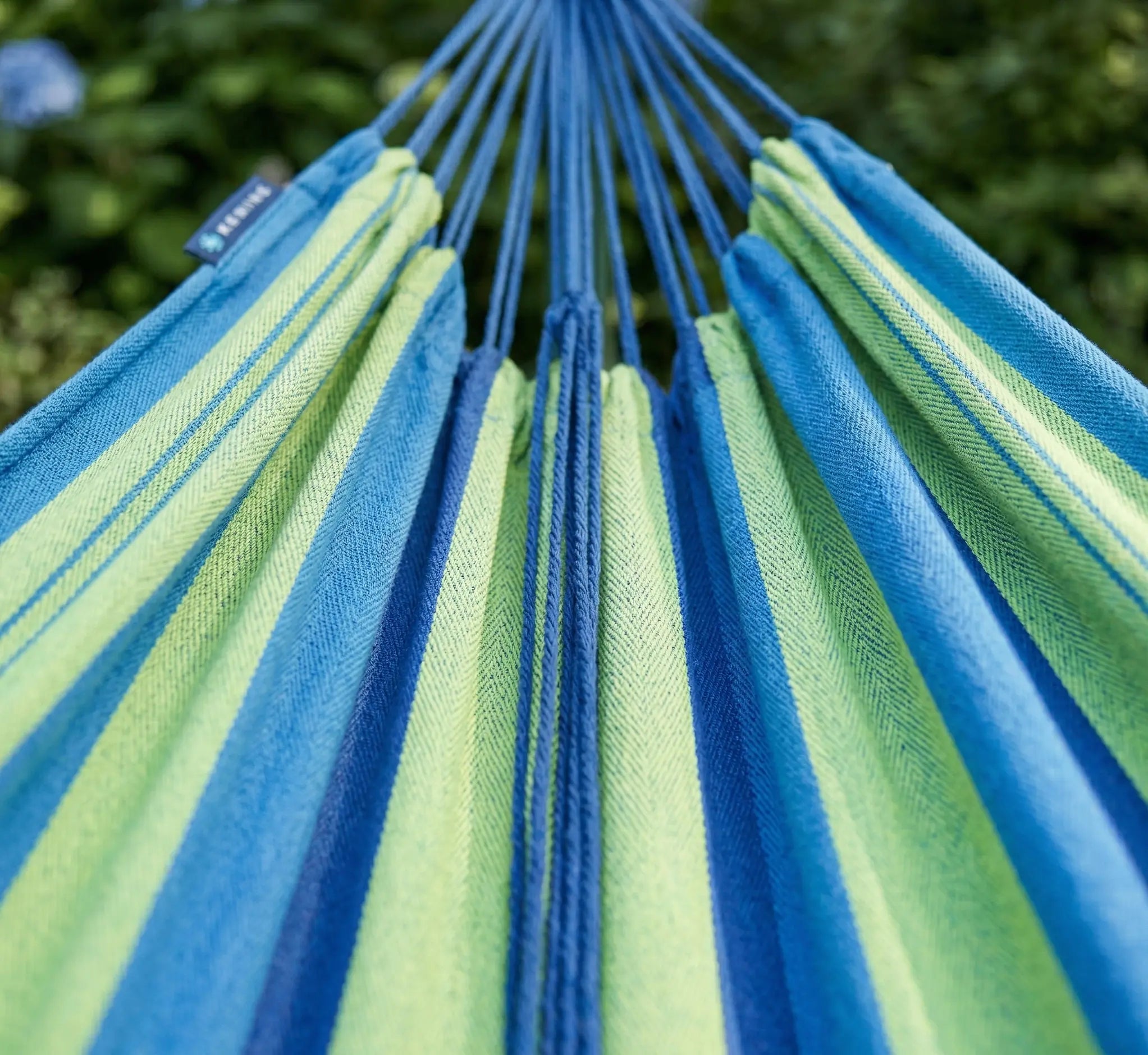Vue en perspective des suspentes bleues et de la toile rayée vert citron et bleu cobalt d'un hamac de luxe montrant la densité du tissage en extérieur