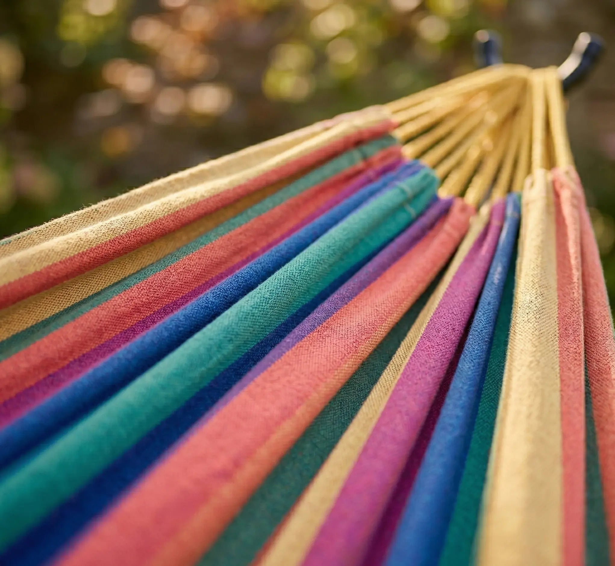 Gros plan sur la texture d'une toile de hamac en coton naturel aux rayures ocre jaune violet et turquoise avec cordes de suspension dans un jardin ensoleillé