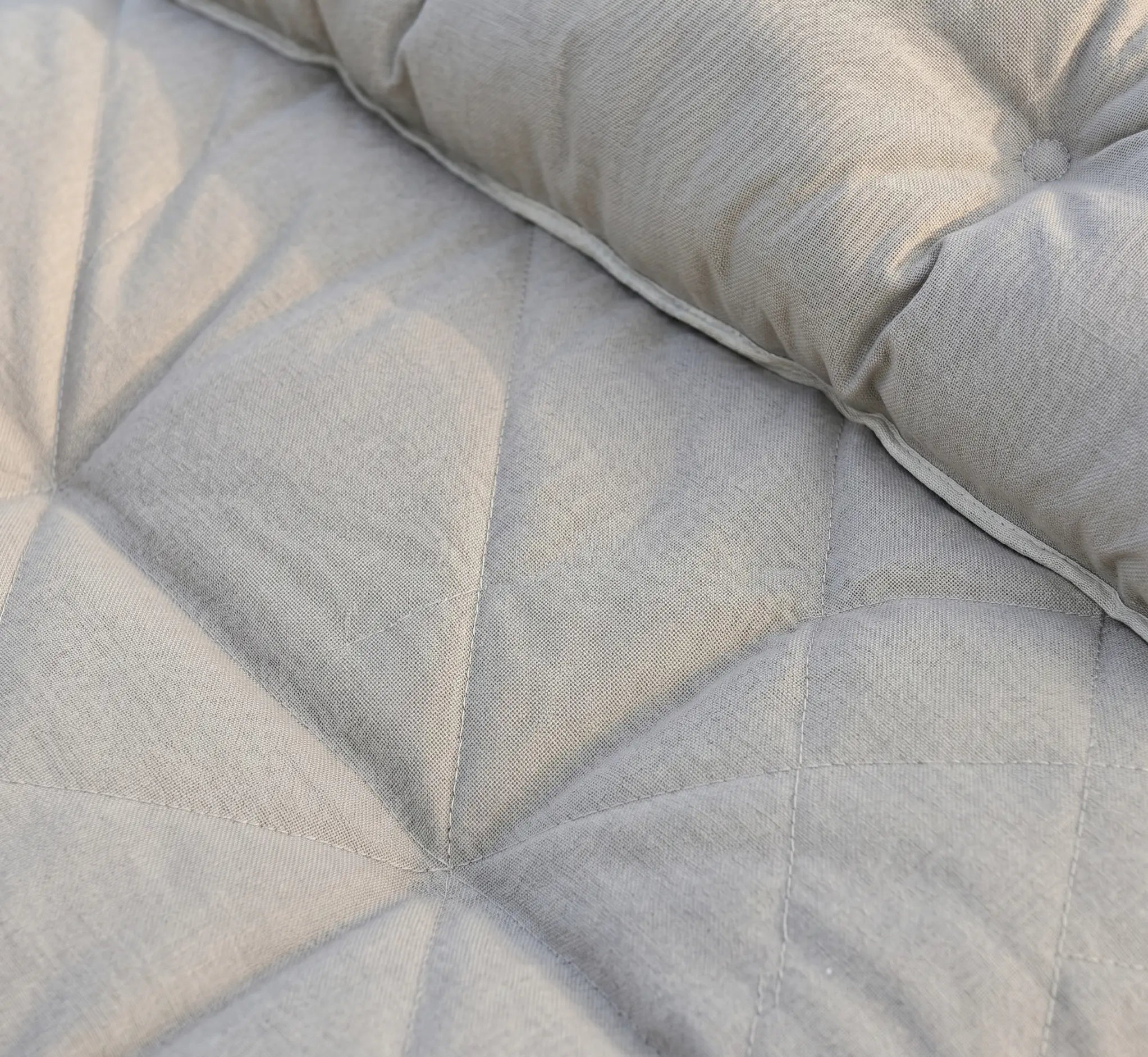 Très gros plan sur le tissu en coton épais d'un hamac rembourré beige, montrant des surpiqûres géométriques en losange et le matelassage moelleux de l'oreiller intégré.