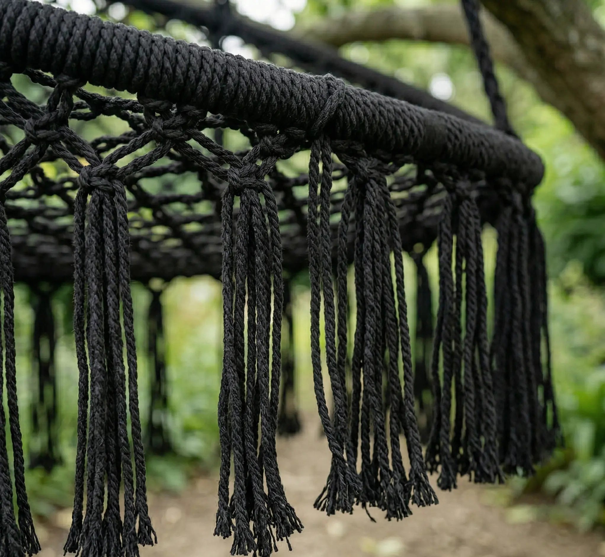 Détail rapproché du tressage en macramé noir d'une balancelle avec franges élégantes montrant la qualité du cordage épais et la finition artisanale